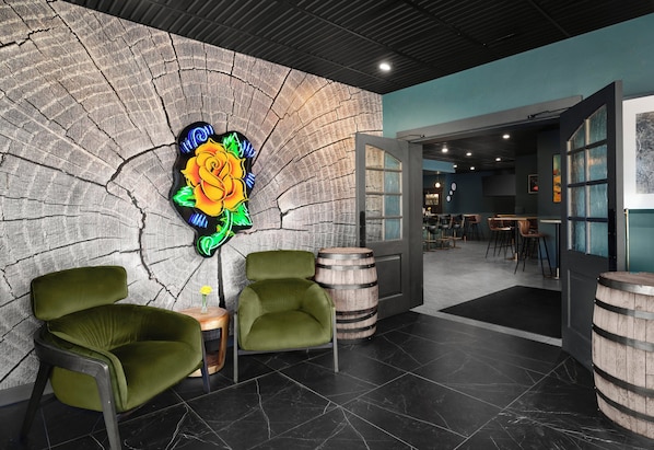 A modern interior with a stone wall, neon art, green chairs, wooden barrels, and a bar area.
