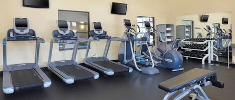 A gym with multiple treadmills, elliptical machines, and a bench press area.