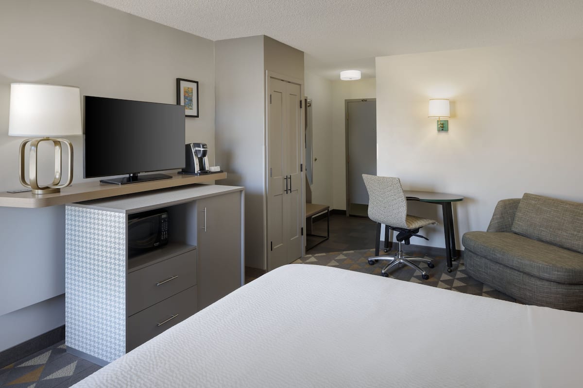 Una habitación de hotel con cama, escritorio, silla, televisor, microondas y armario.