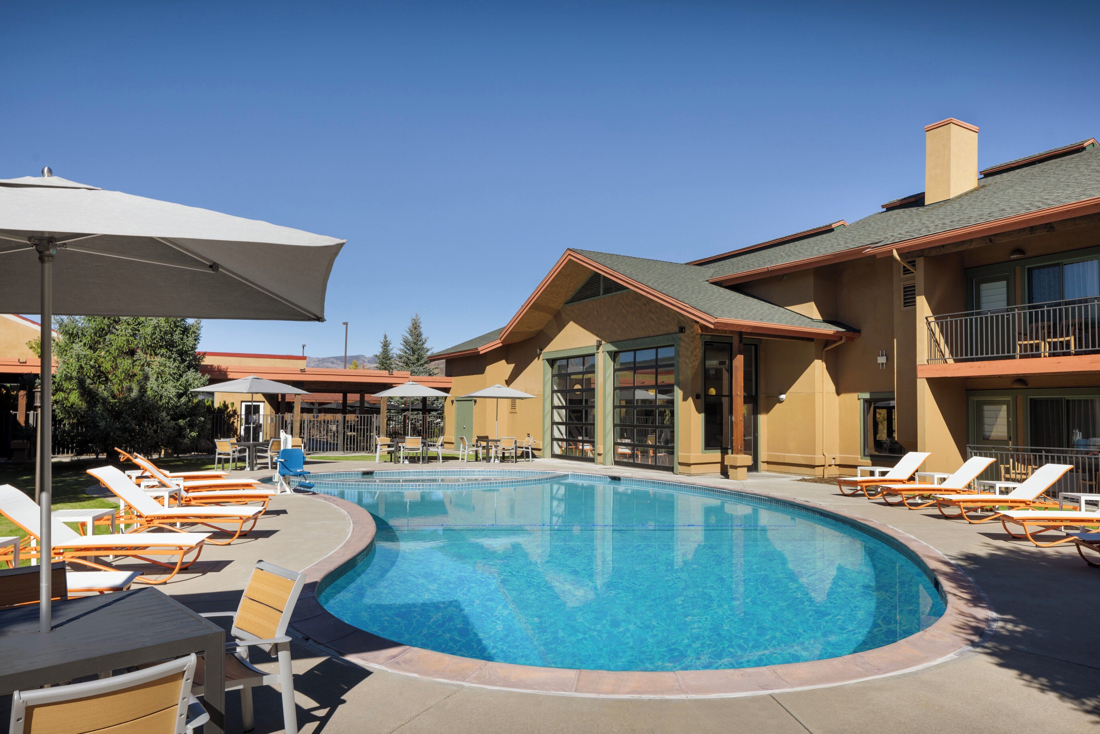 A swimming pool with lounge chairs and umbrellas, surrounded by buildings with large windows and balconies.