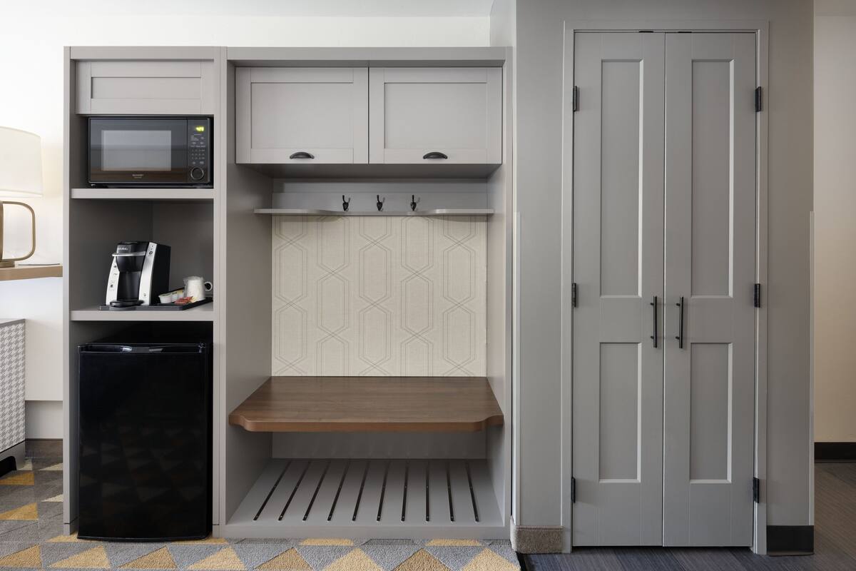 Una kitchenette compacta con microondas, cafetera y una banca integrada.