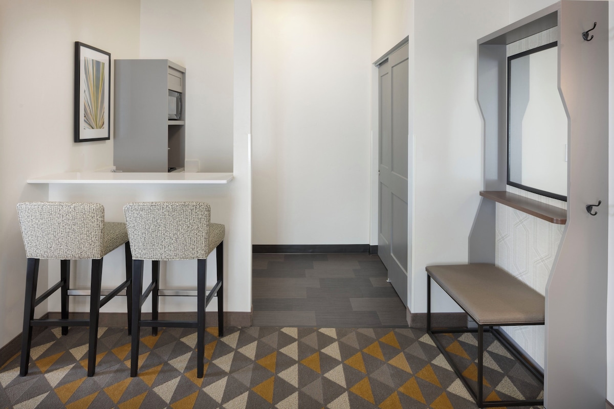 A hallway with a patterned carpet, two bar stools, a bench, a door, and a framed picture on the wall.