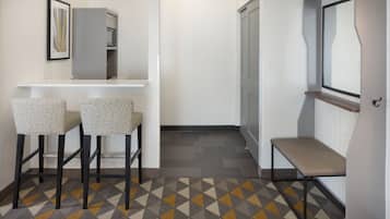Un pasillo con alfombra estampada, dos taburetes de bar, un banco, una puerta y un cuadro en la pared.