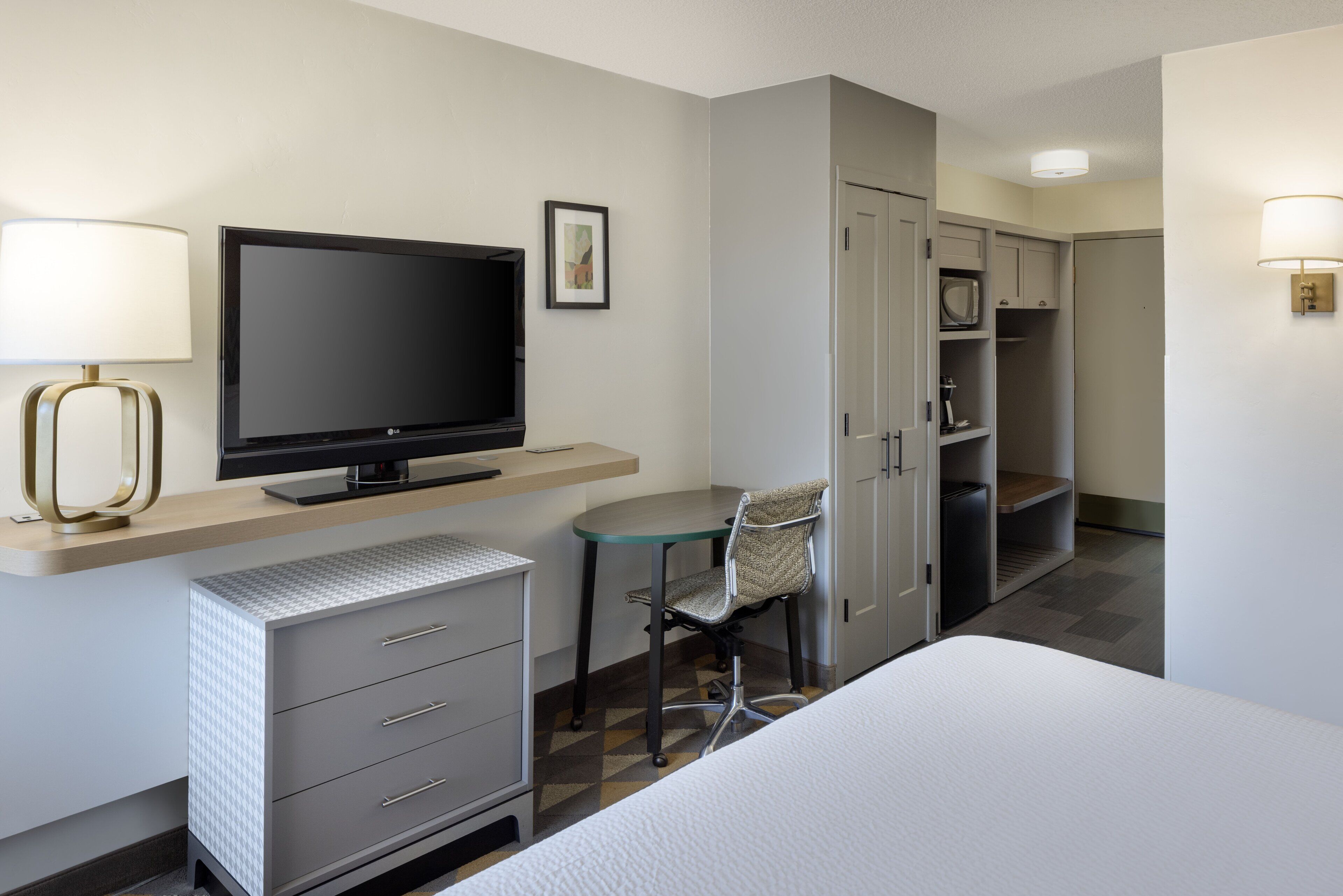 Une chambre d’hôtel comprenant un lit, un bureau avec une télévision, une chaise, une armoire et un four à micro-ondes.