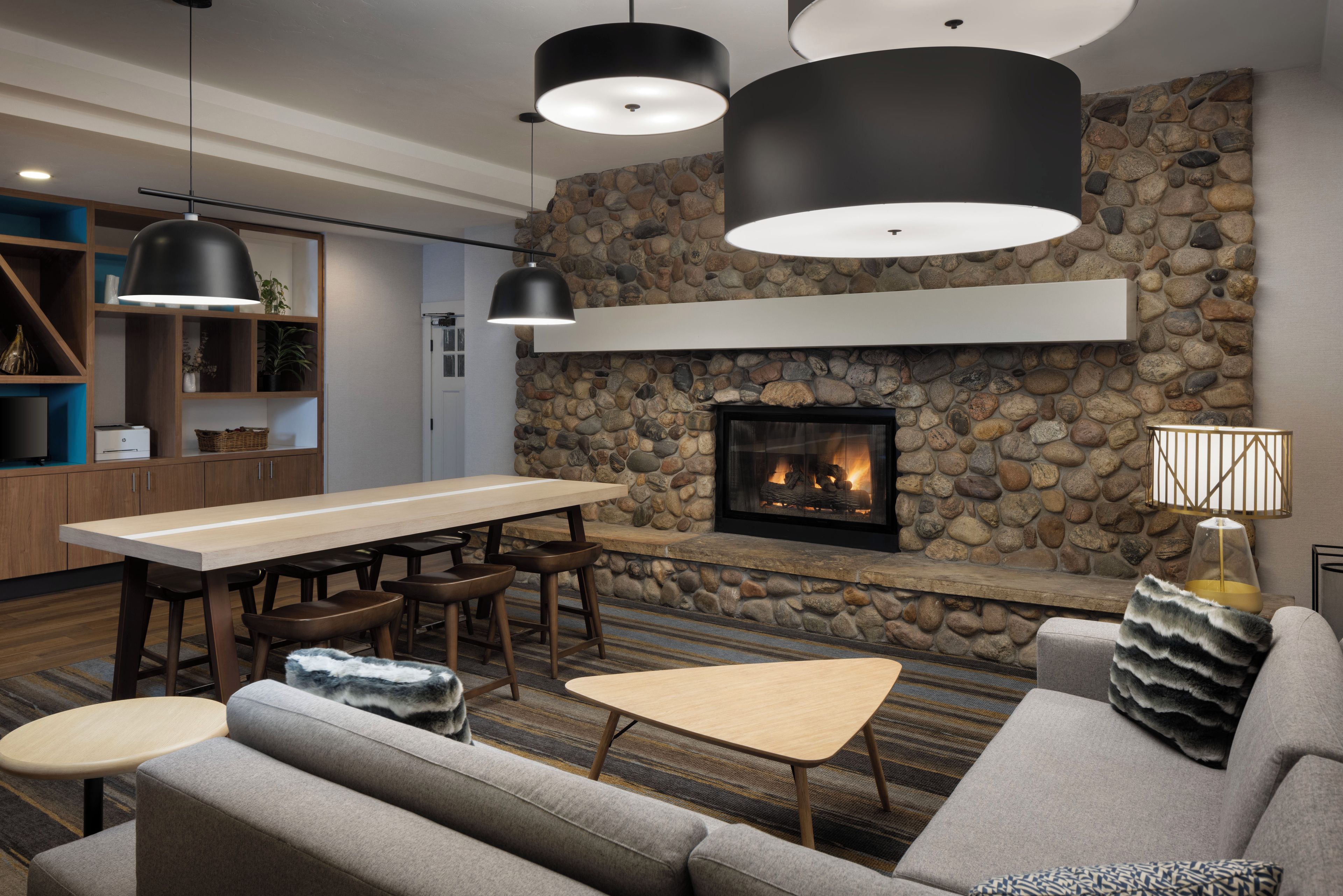 A modern living room with a stone fireplace, wooden furniture, and pendant lighting.