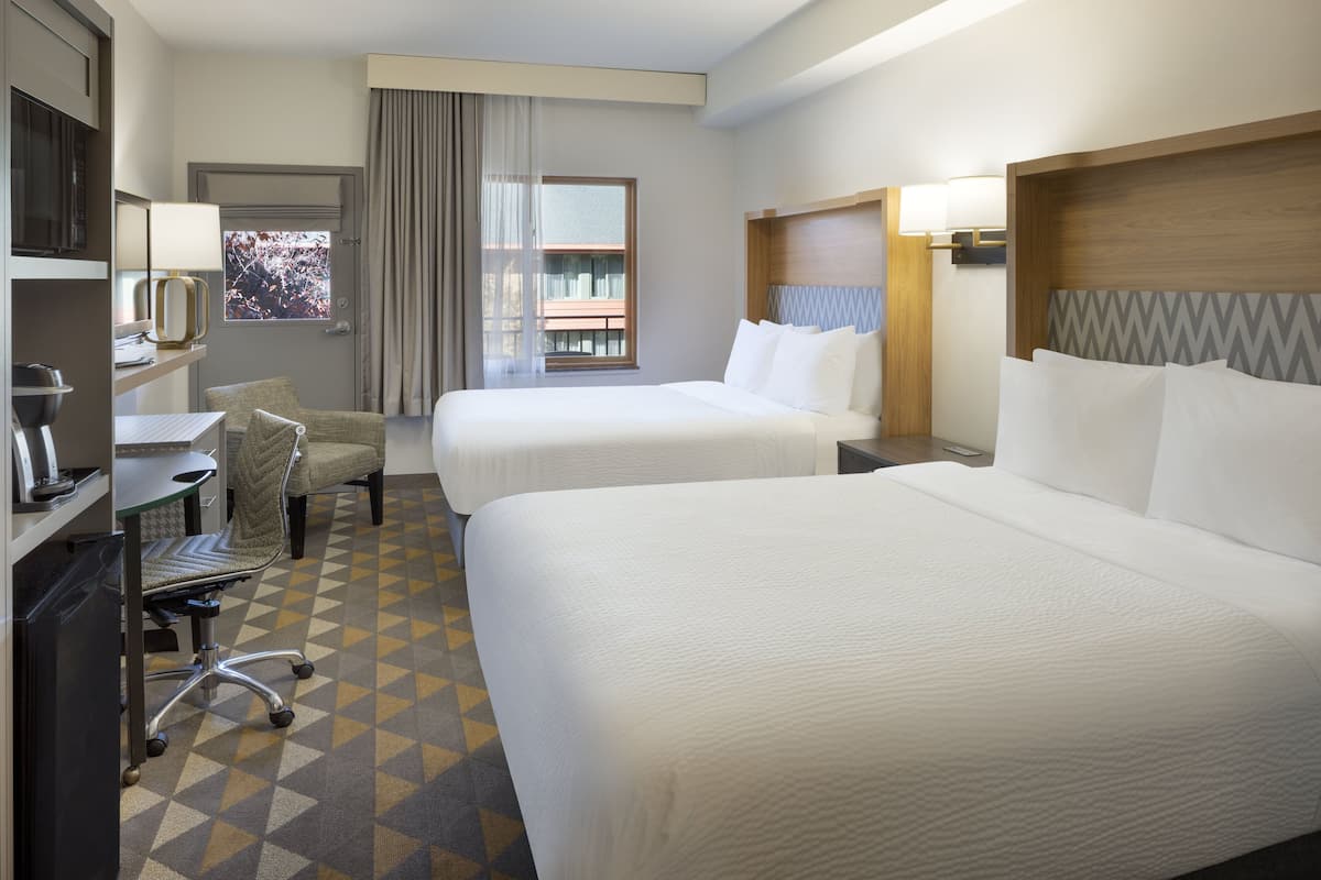 Habitación de hotel con dos camas, un escritorio con silla, un televisor y ventana con vistas al exterior.