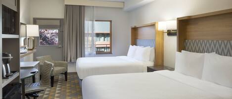 Ein Hotelzimmer mit zwei Betten, einem Schreibtisch mit Stuhl, einem Fernseher und einem Fenster mit Ausblick.