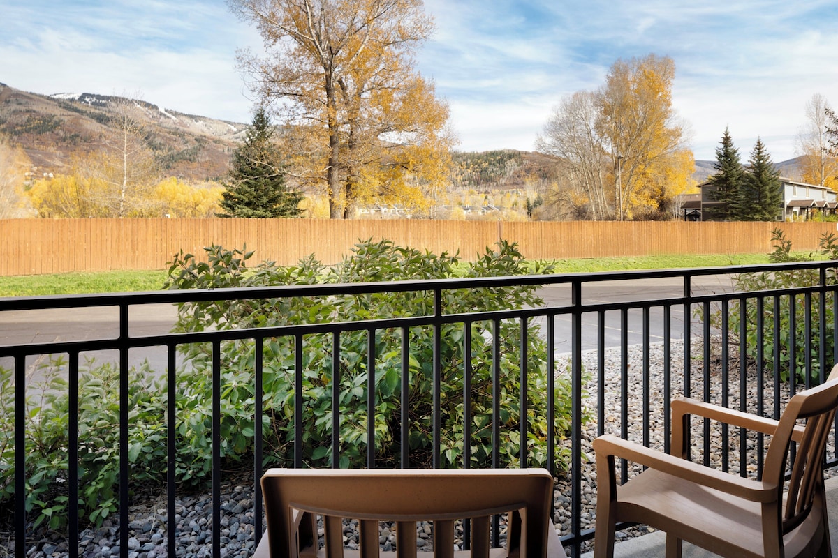 A balcony with a view of a wooden fence, greenery, and distant houses.