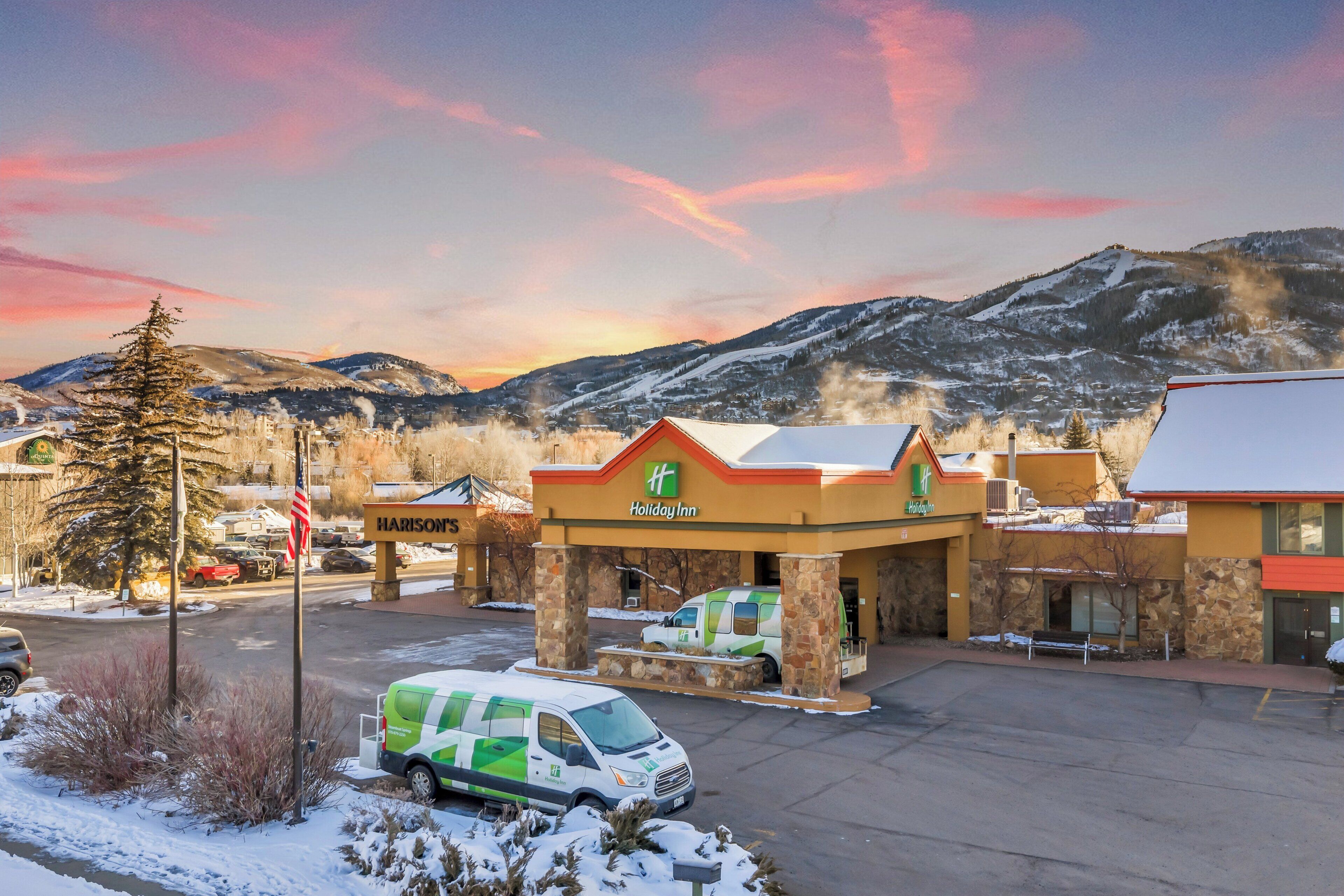 A Holiday Inn with a stone facade, a parking lot, and a mountainous backdrop.