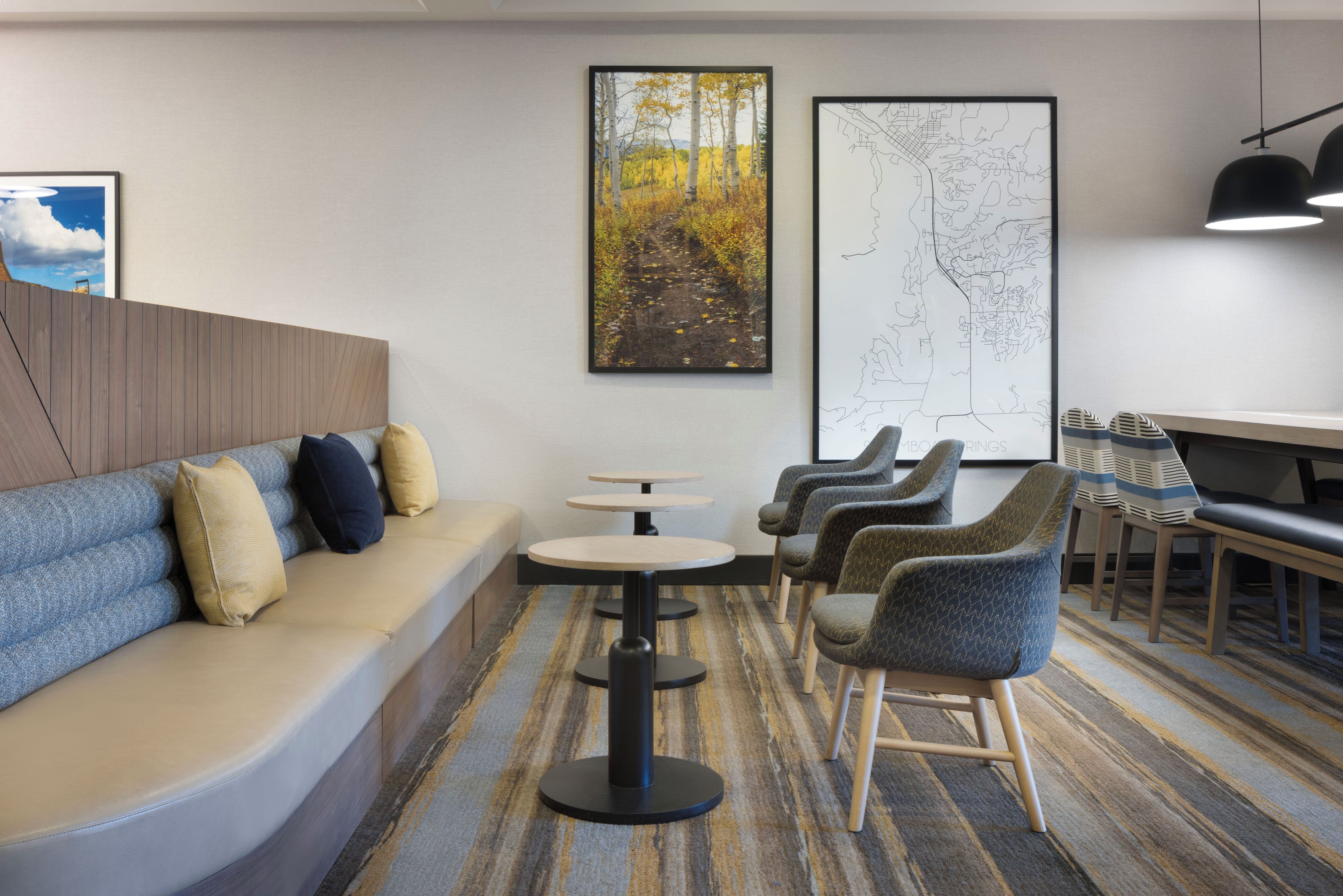 A modern lounge area with a sofa, chairs, a small table, and artwork on the walls.
