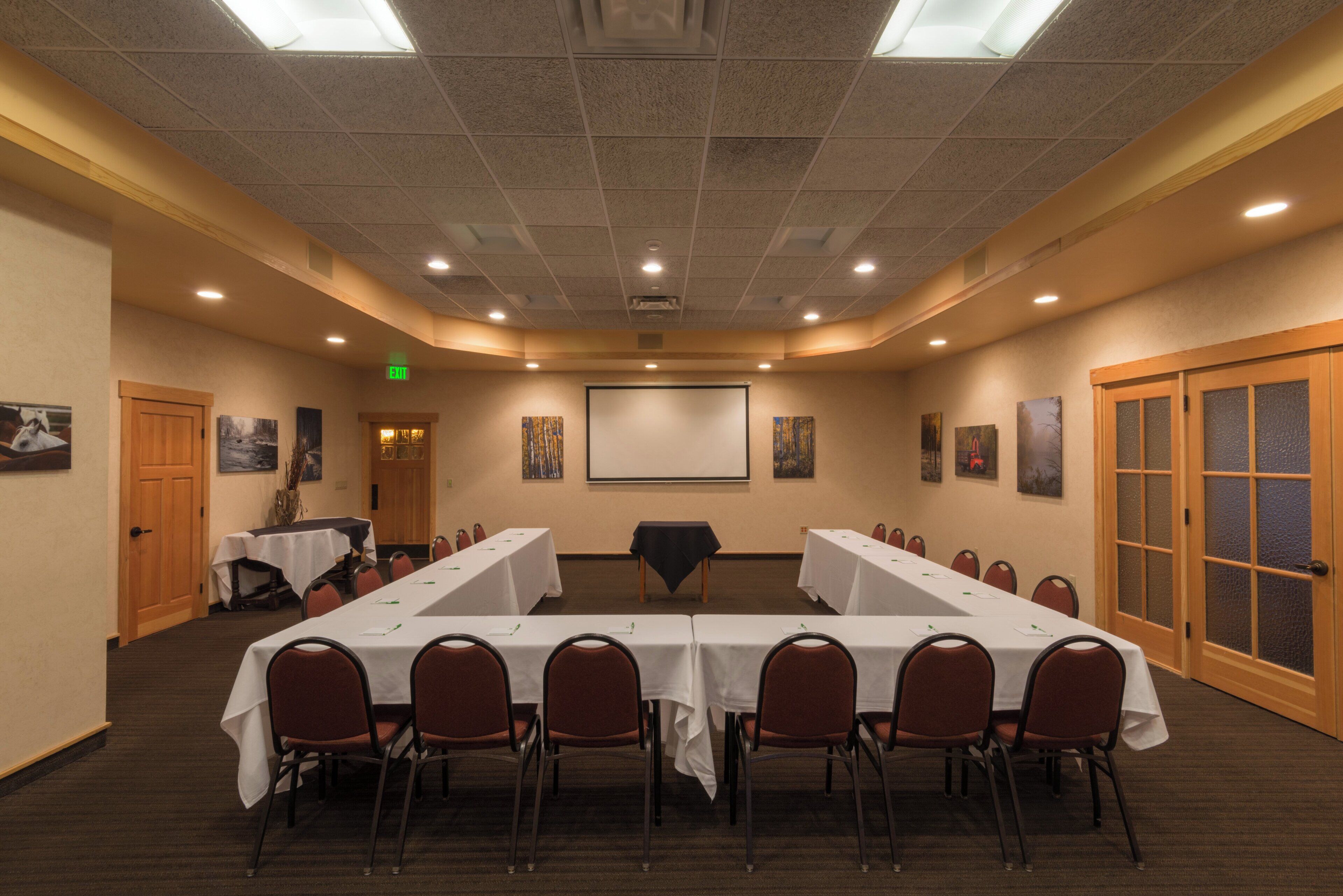 A conference room with a long table, chairs, a projector screen, and artwork on the walls.