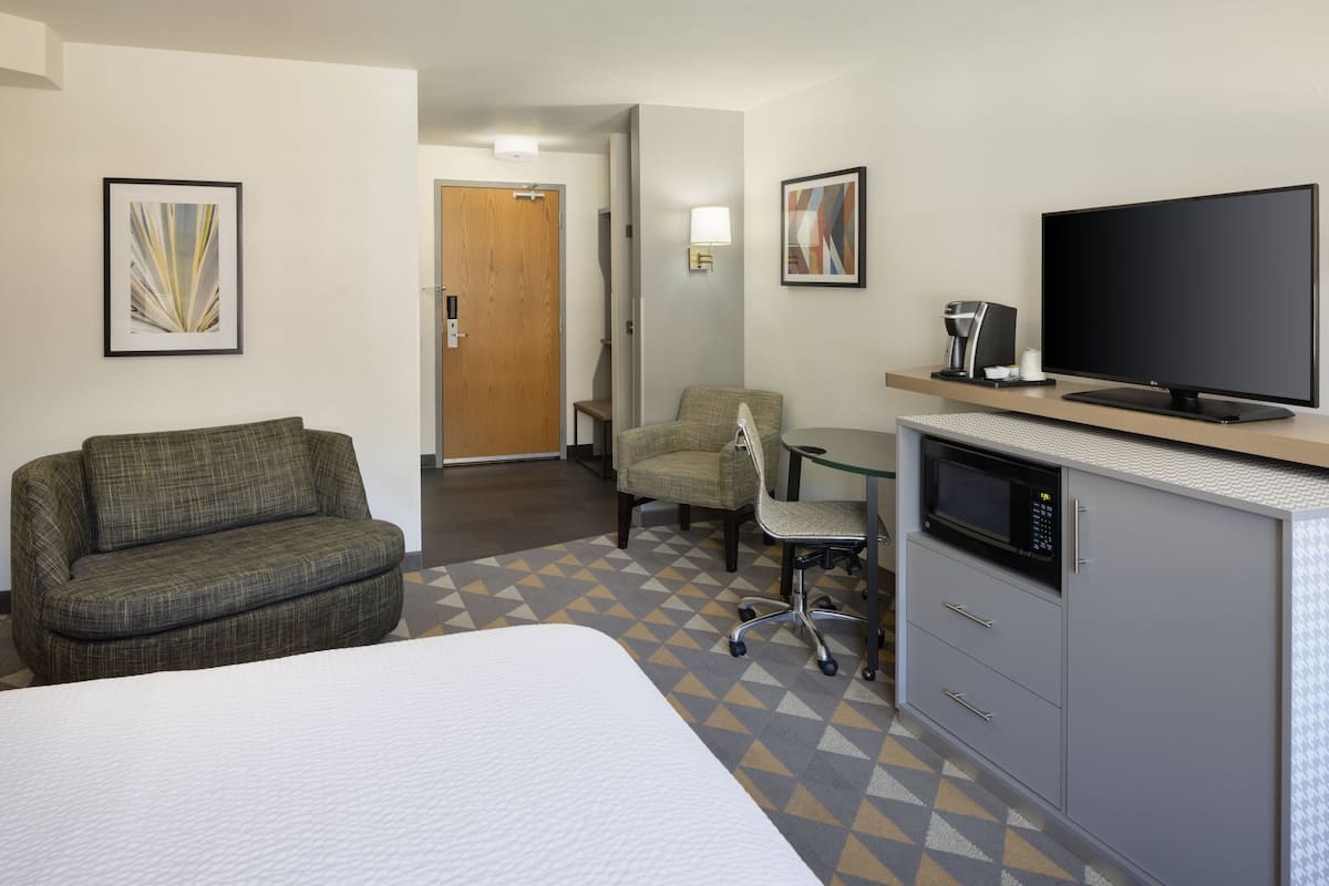 Una habitación de hotel con cama, sofá, escritorio con computadora, televisión y microondas.