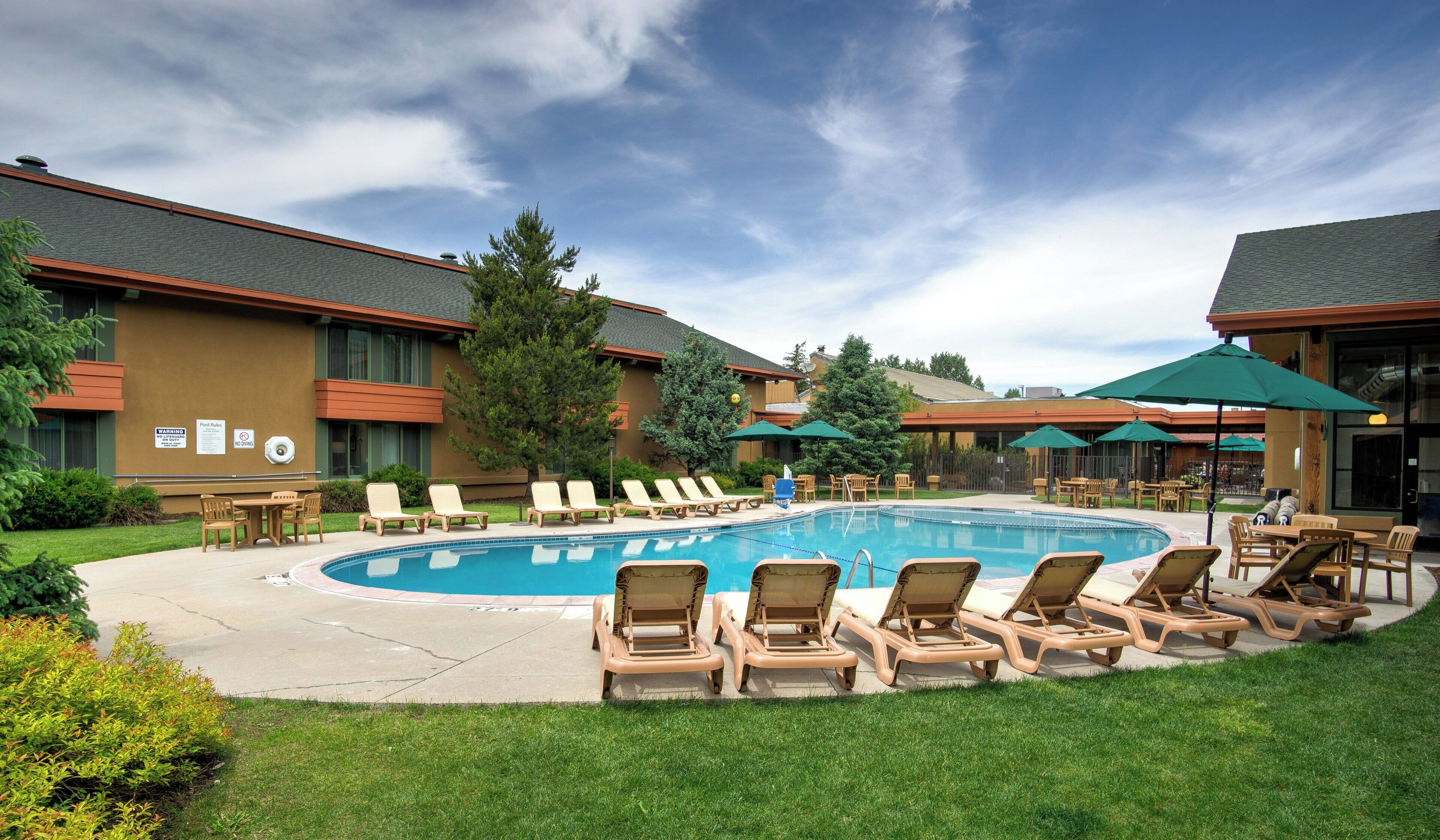 Un hotel con piscina, sillas de descanso y mobiliario exterior.