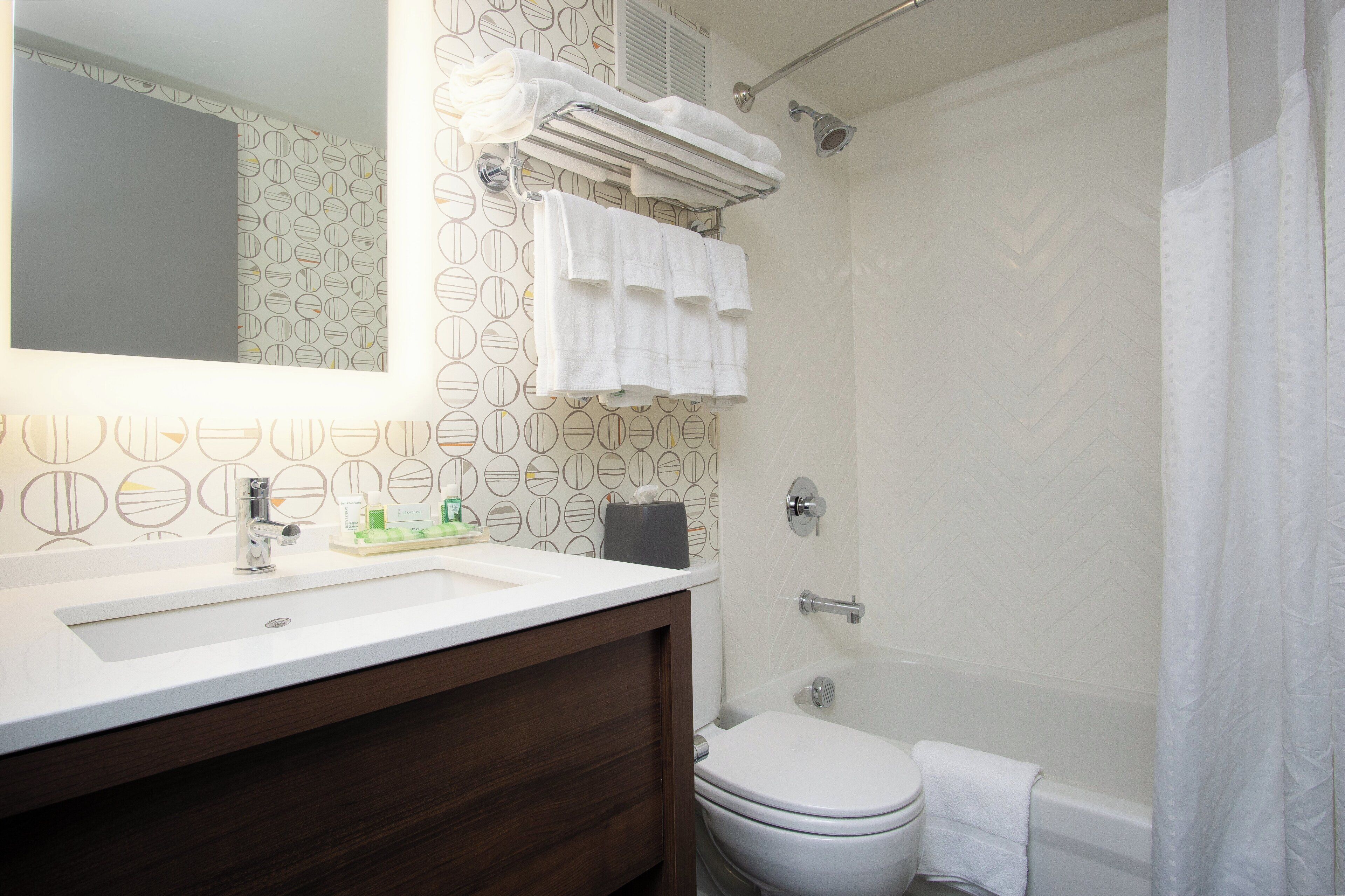 A bathroom with a white sink, a toilet, a shower with a curtain, and a mirror with a towel rack.