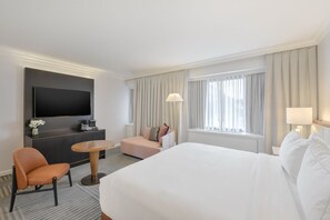 A hotel room with a bed, a desk, a TV, a chair, and a window with curtains. - Capital Hilton (Washington)