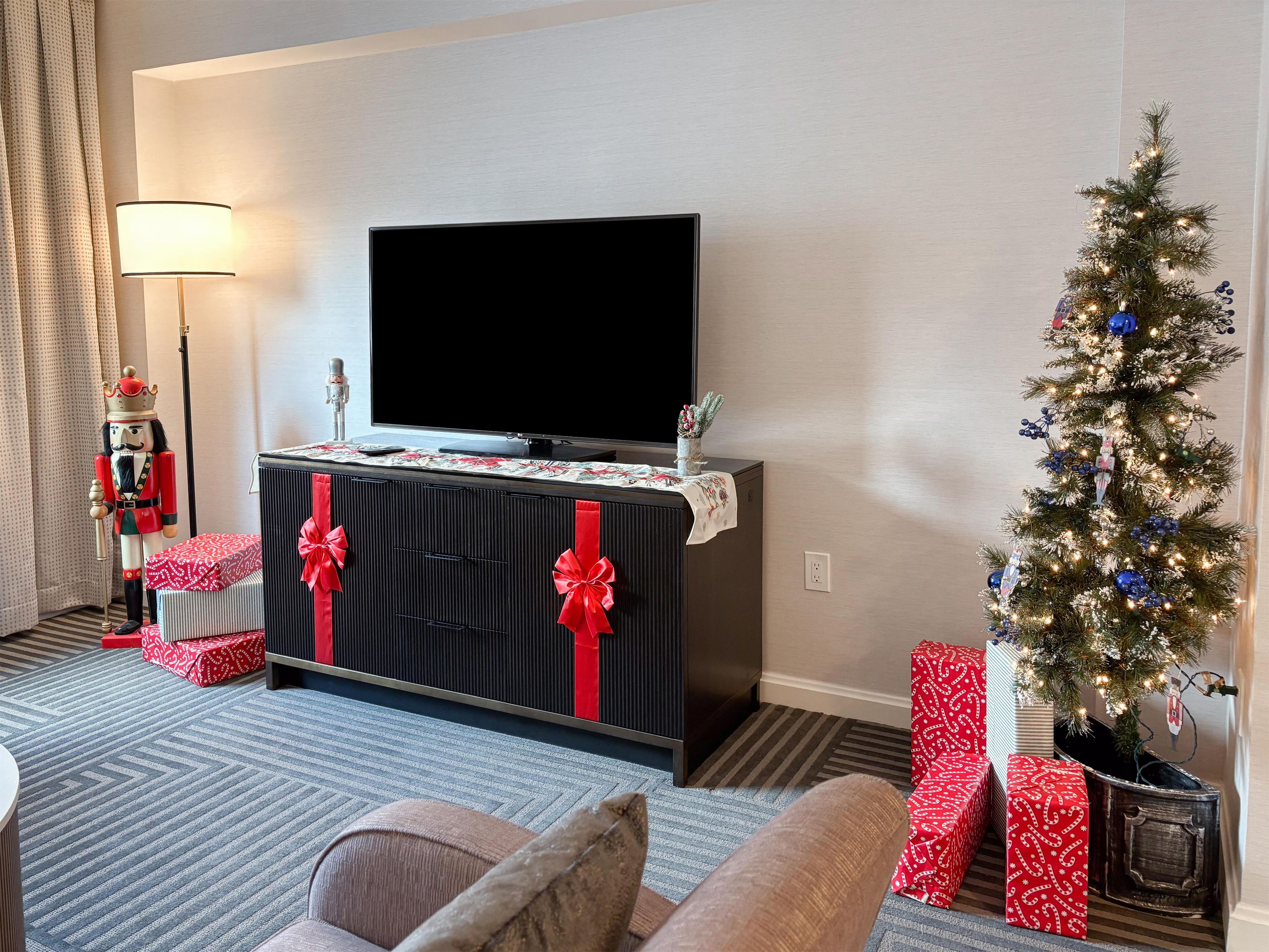 A hotel room with a flat-screen TV, a Christmas tree, and red gift boxes.
