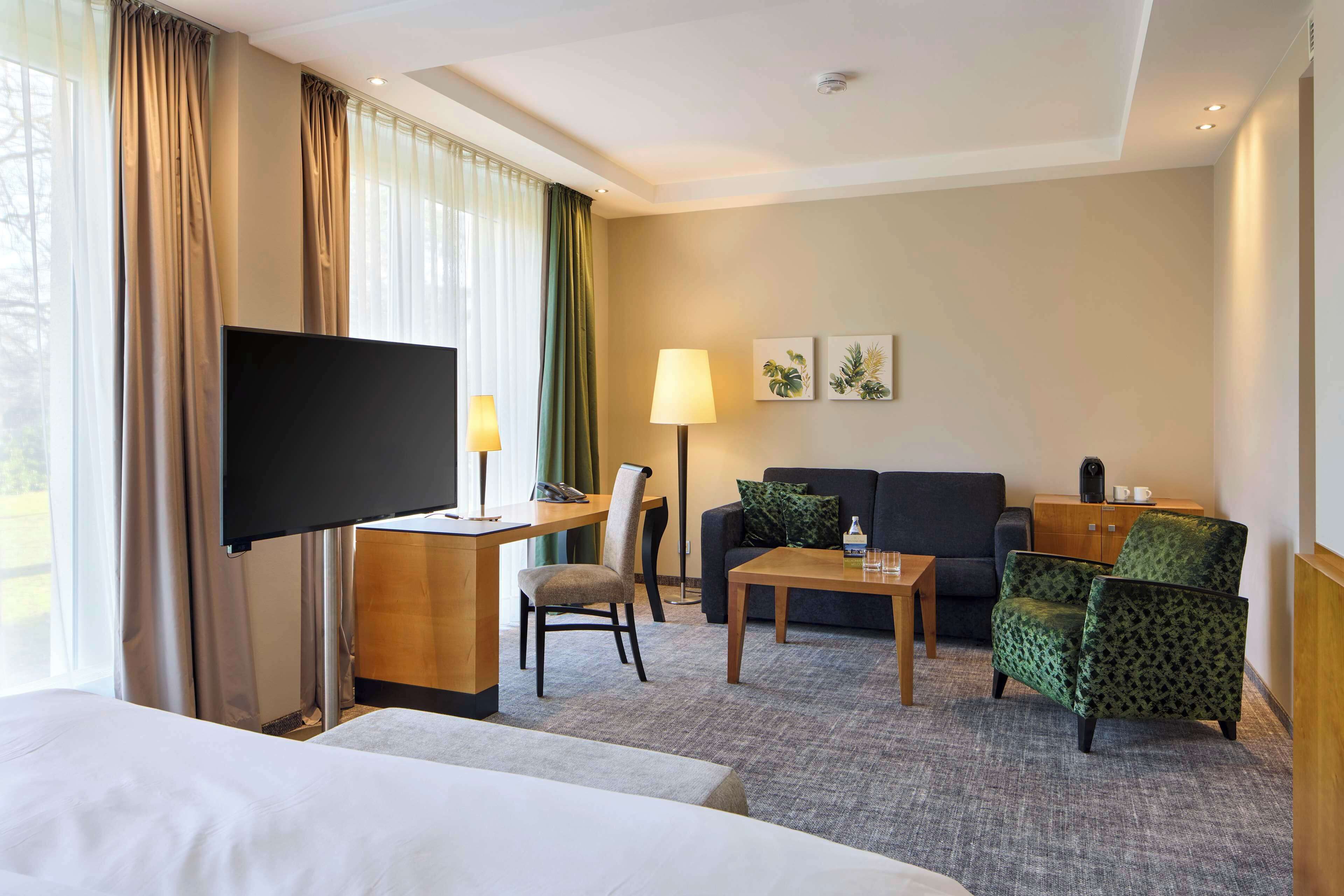 Una habitación de hotel con una cama, un escritorio con televisor de pantalla plana, un sofá, una silla, una mesa de centro y una lámpara.