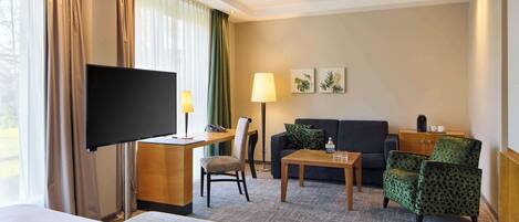 Una habitación de hotel con una cama, un escritorio con televisor de pantalla plana, un sofá, una silla, una mesa de centro y una lámpara.