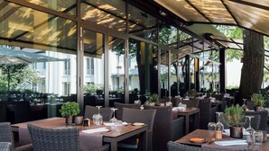 An outdoor dining area with wicker furniture, glass tables, and umbrellas. - Best Western Premier Park Hotel and Spa (Bad Lippspringe)