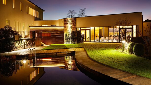 A modern building with a swimming pool, a stone wall, and a well-lit entrance. - Best Western Premier Park Hotel and Spa (Bad Lippspringe)