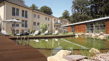 Een zwembad met ligbedden en een houten terras, omringd door een gebouw met grote ramen en een modern ontwerp.