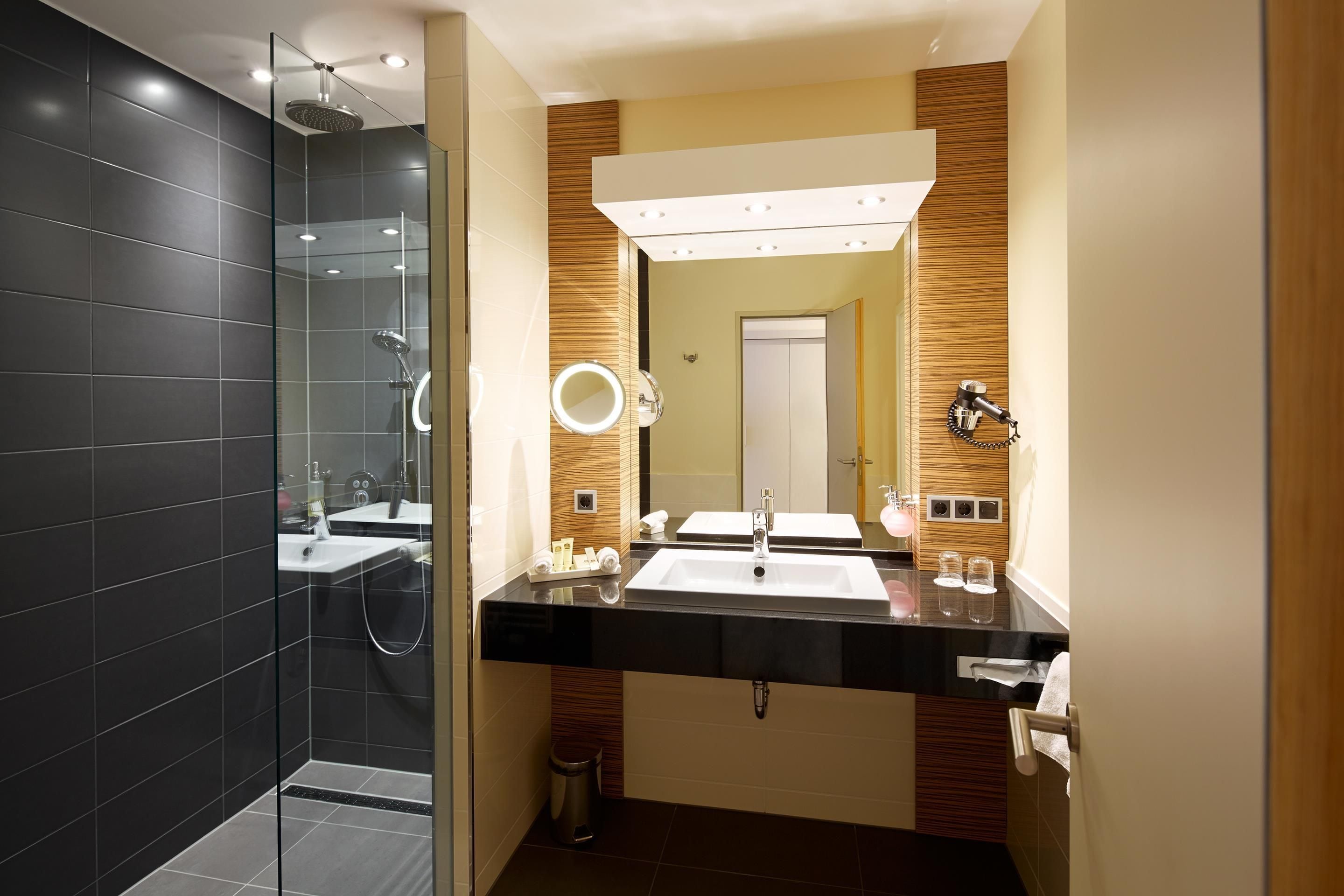 A modern bathroom with a glass-enclosed shower, two sinks, a vanity with a mirror, and a towel rack.
