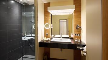A modern bathroom with a glass-enclosed shower, two sinks, a vanity with a mirror, and a towel rack.