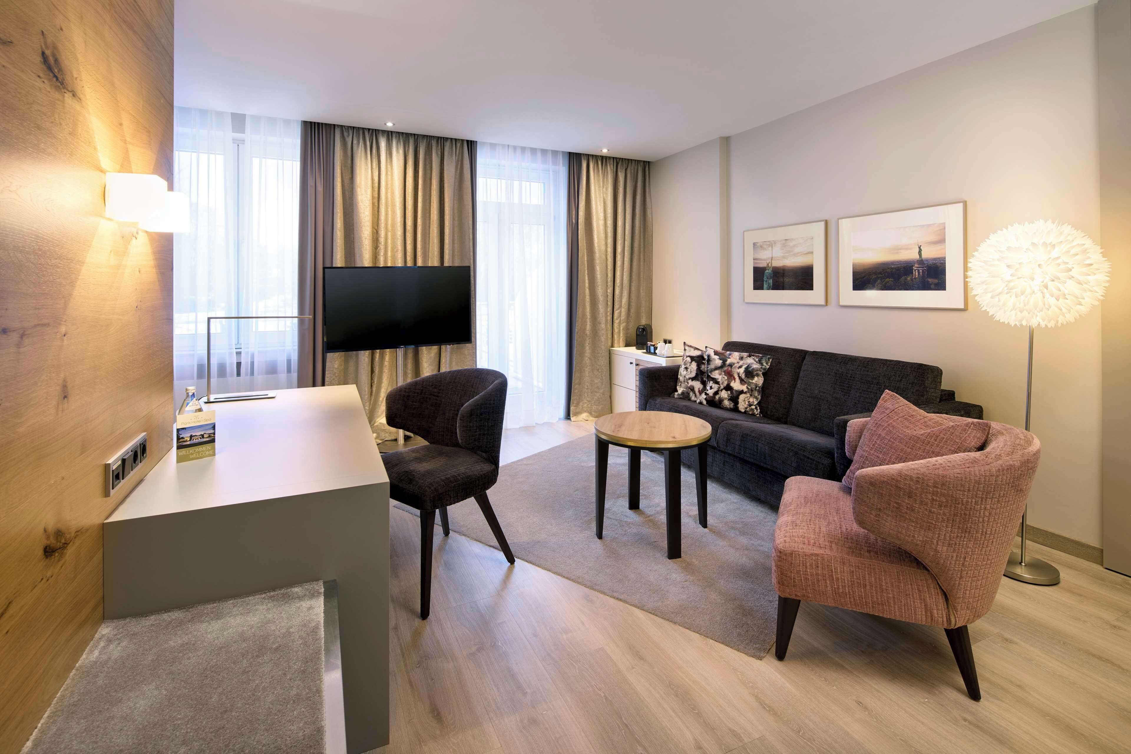 Une chambre d’hôtel moderne équipée d’un téléviseur à écran plat, d’un canapé, de deux fauteuils, d’une petite table basse et d’une lampe.