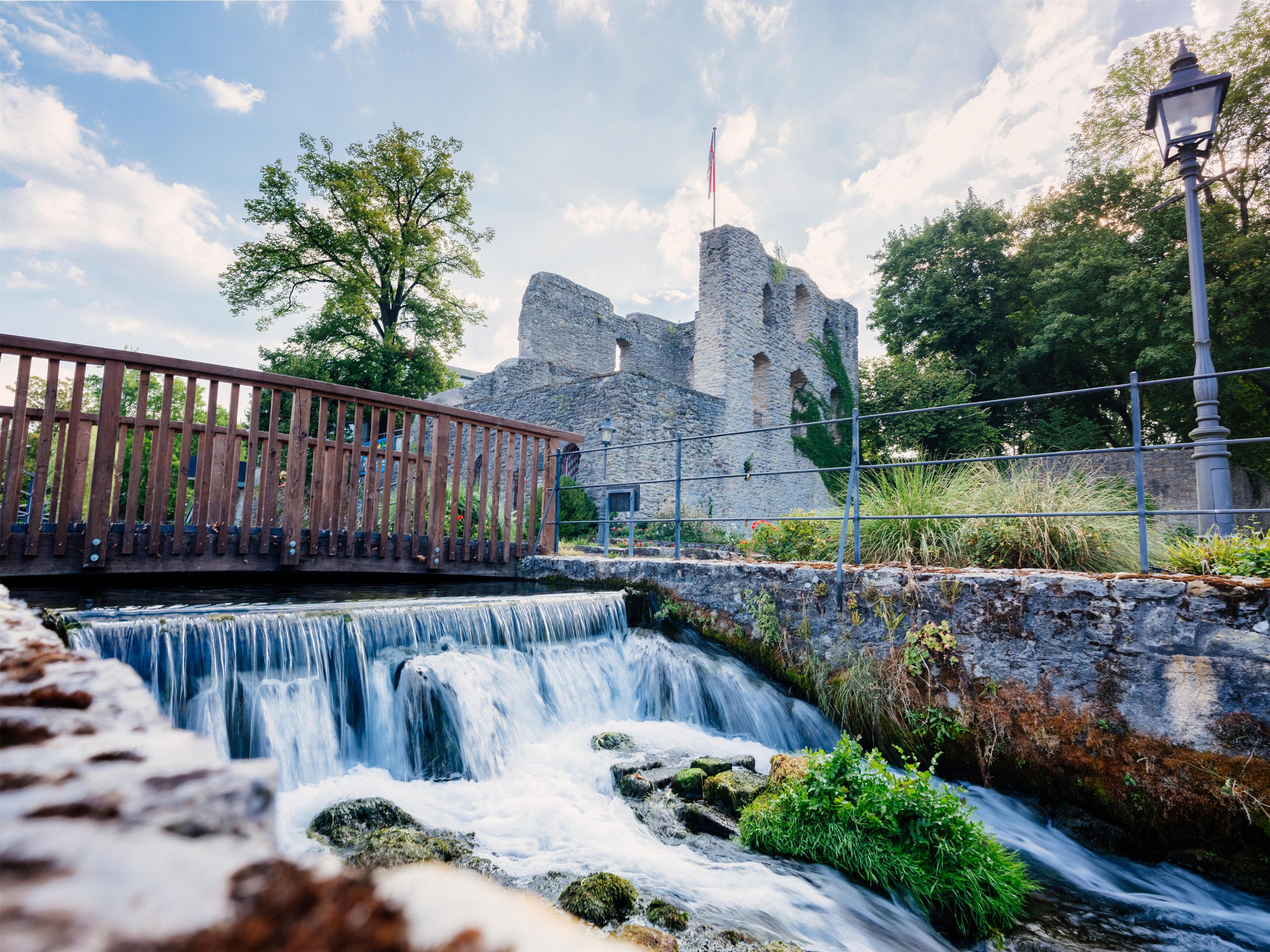 A stone bridge over a waterfall, a stone wall, and a flagpole with a flag.