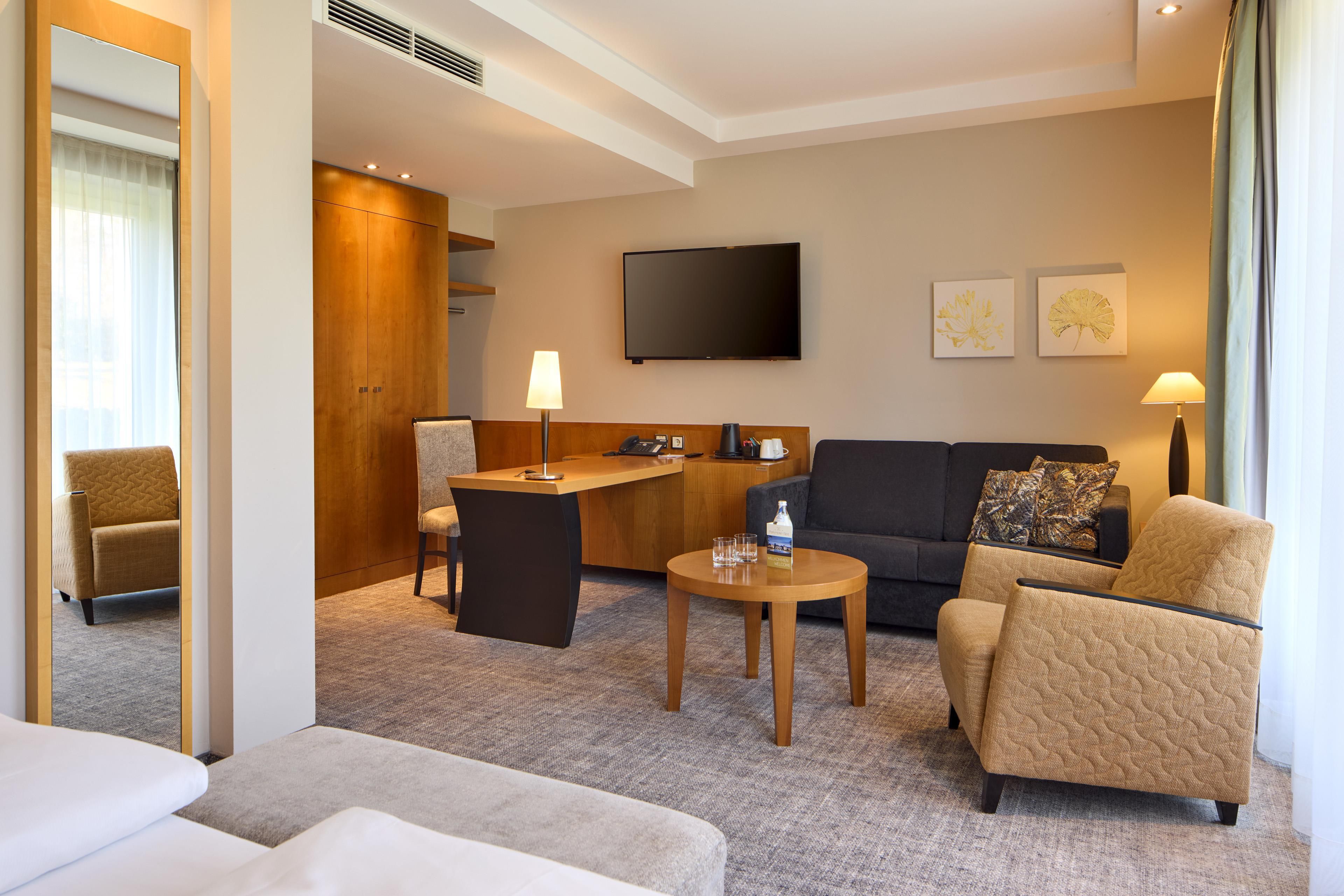 A hotel room with a sofa, armchair, desk, and a television.