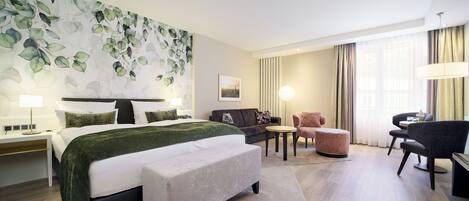 Una habitación de hotel con cama, escritorio, silla, sofá y una pared con diseño de hojas.