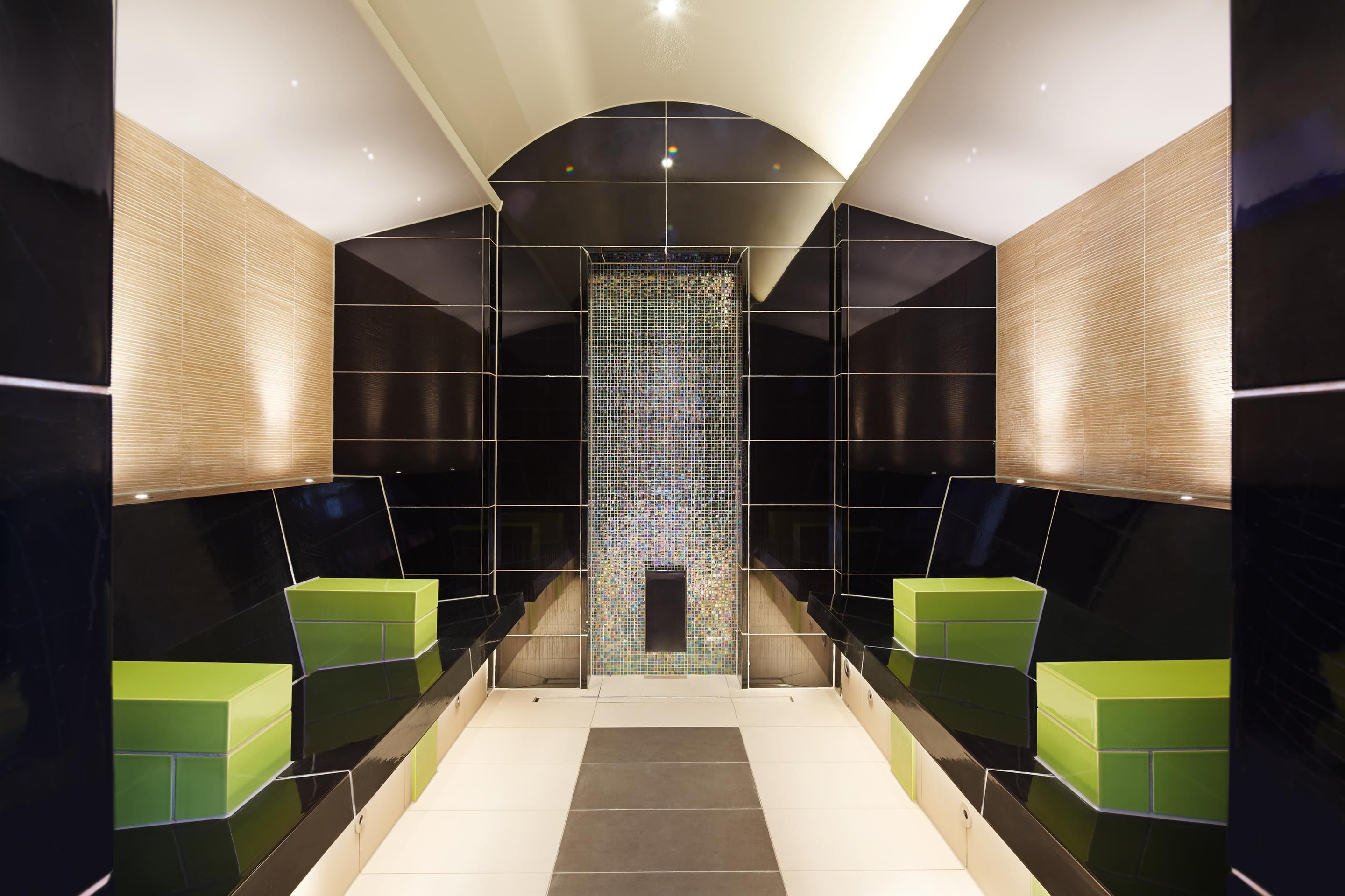 A modern bathroom with a central mirror, black and green tiles, and a geometric design.
