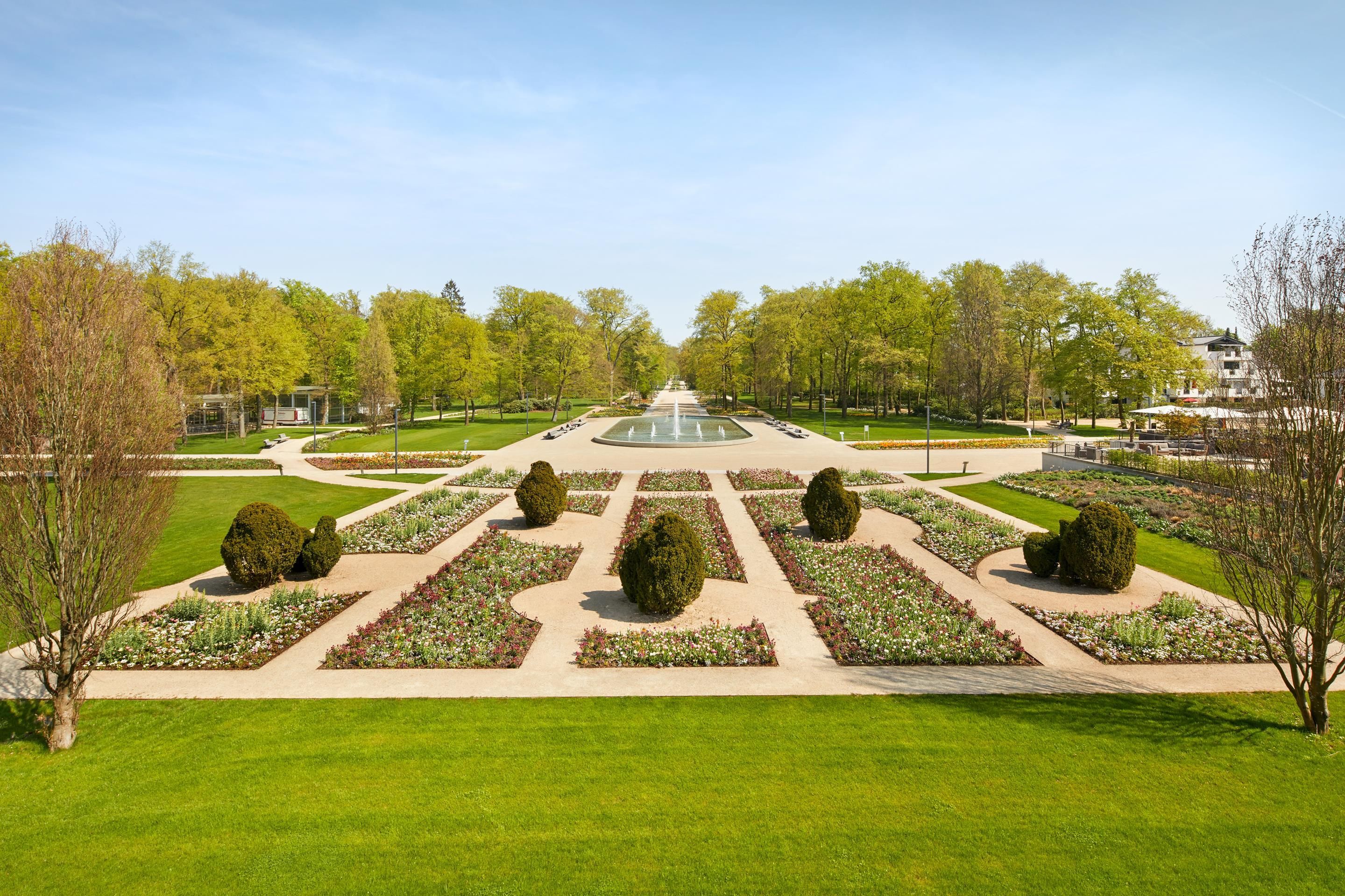 A formal garden with a central fountain, symmetrical pathways, and neatly trimmed hedges.
