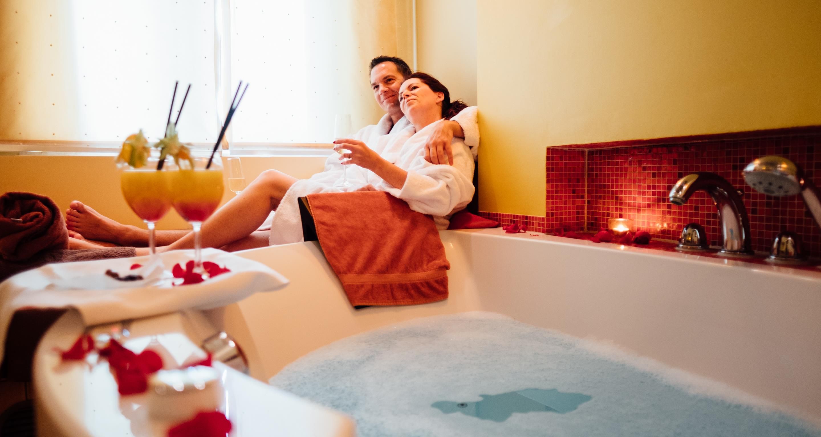 A couple relaxing in a bathtub with rose petals and a glass of wine.