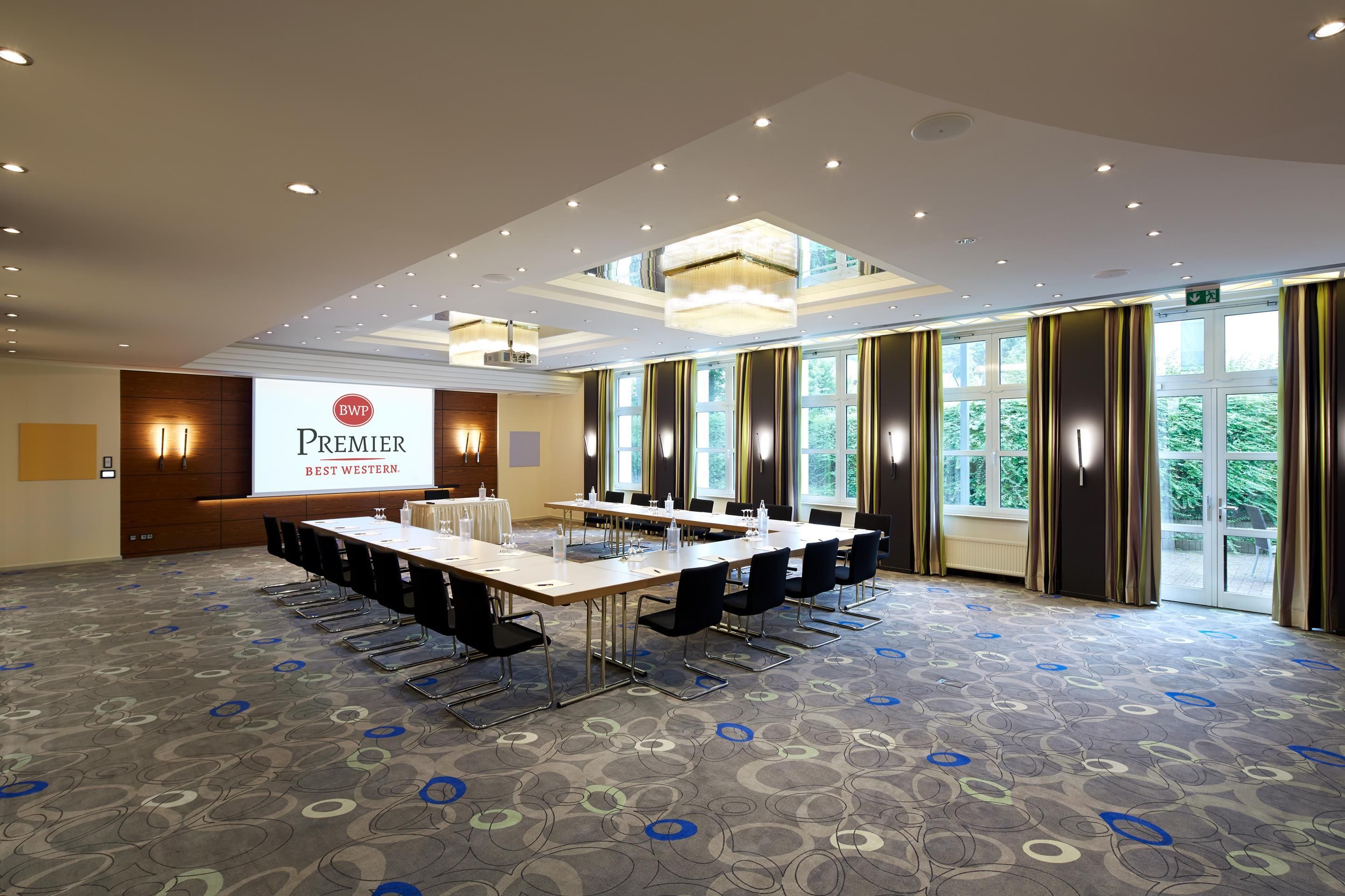 A conference room with a long table, chairs, a projector screen, and a large window with curtains.