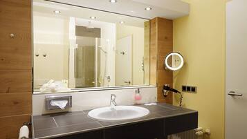 A bathroom with a large mirror, a sink, a towel rack, and a shower.