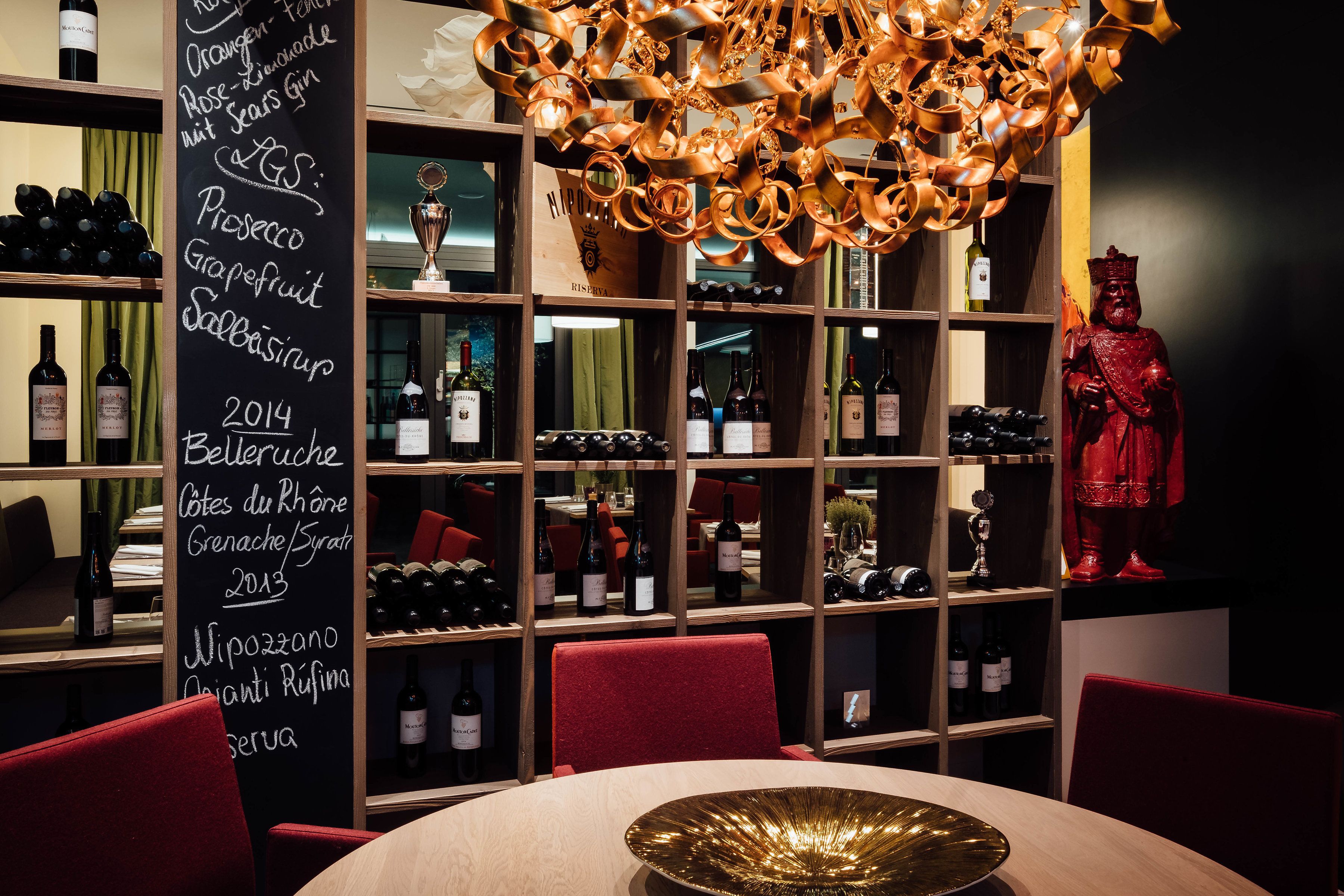 Ein Restaurantinneres mit Weinkühlschrank, einer roten Statue und einer Kreidetafel-Speisekarte.