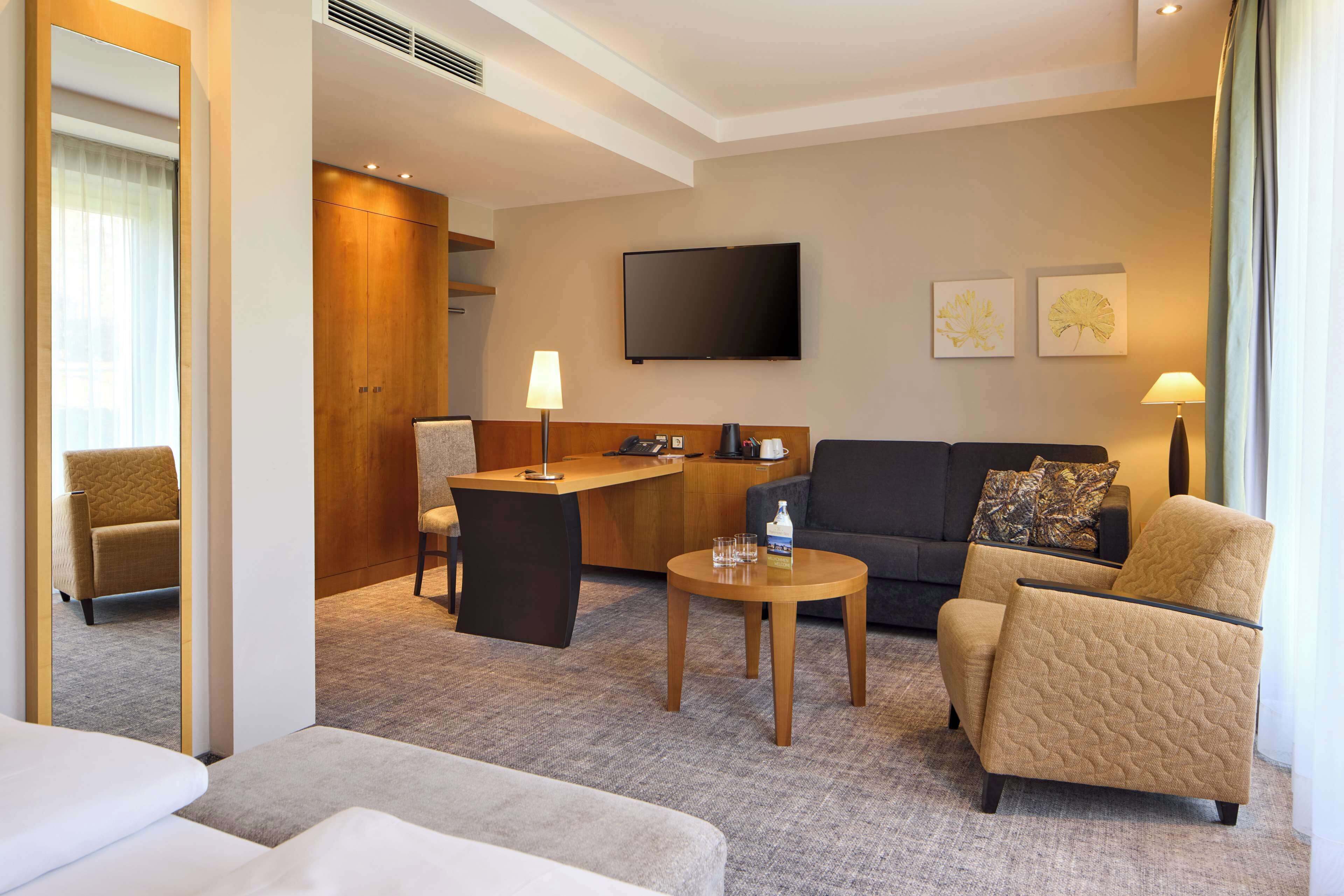 A hotel room with a sofa, armchair, desk, and a television.