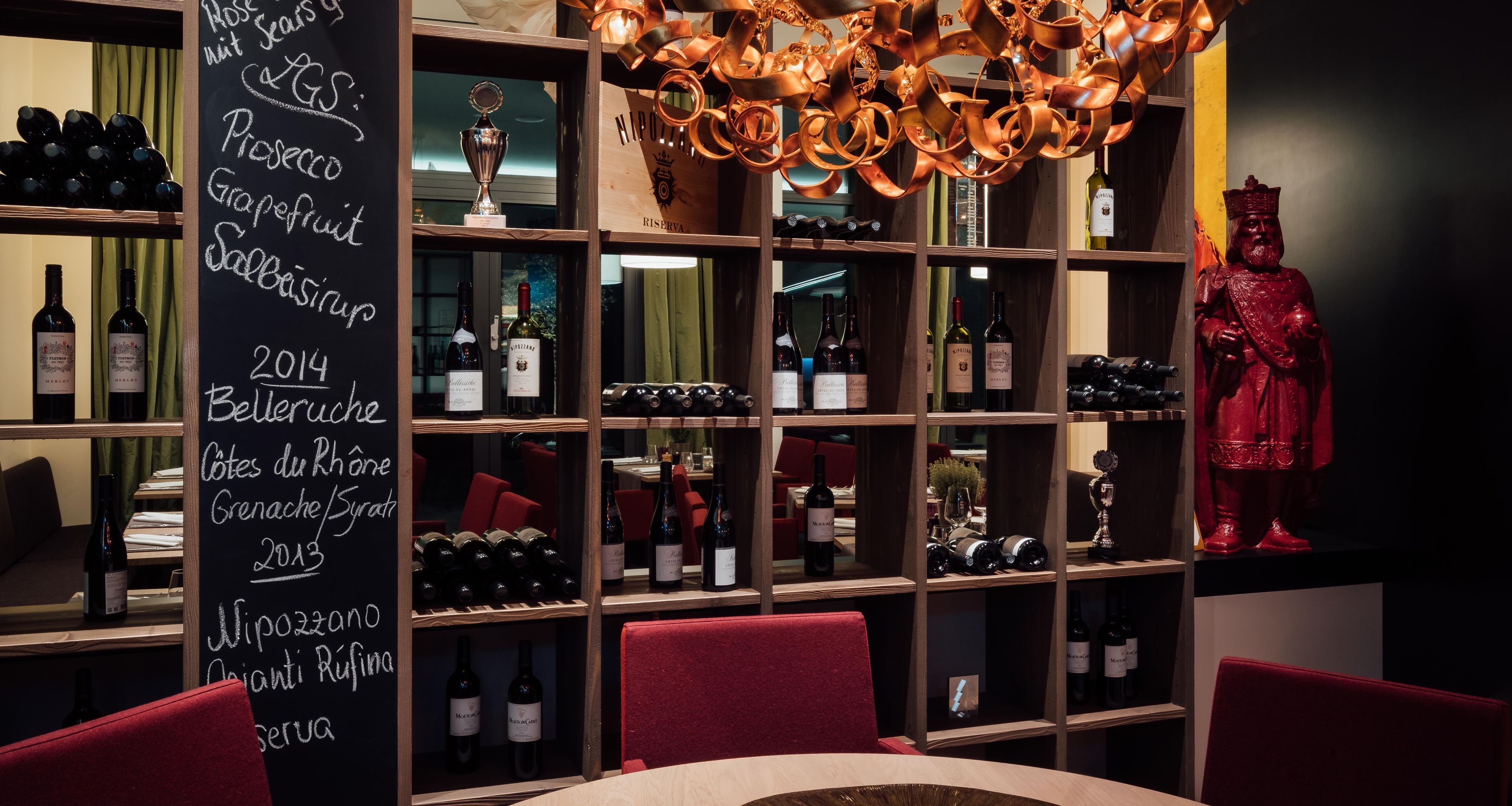 A wine cellar with shelves of wine bottles, a chalkboard with wine information, and a statue.