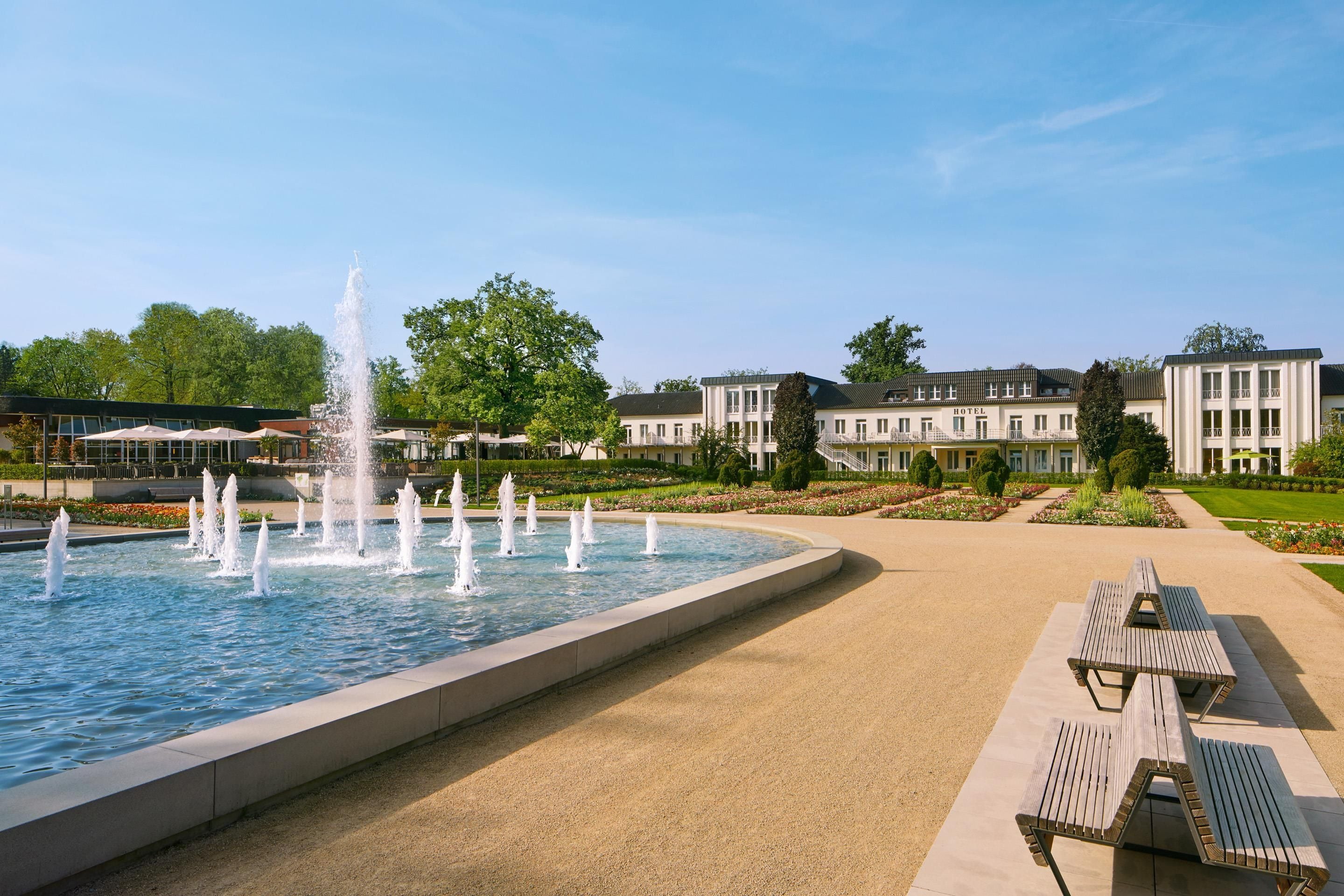 Een hotel met een grote fontein, terras en keurig onderhouden tuinen.