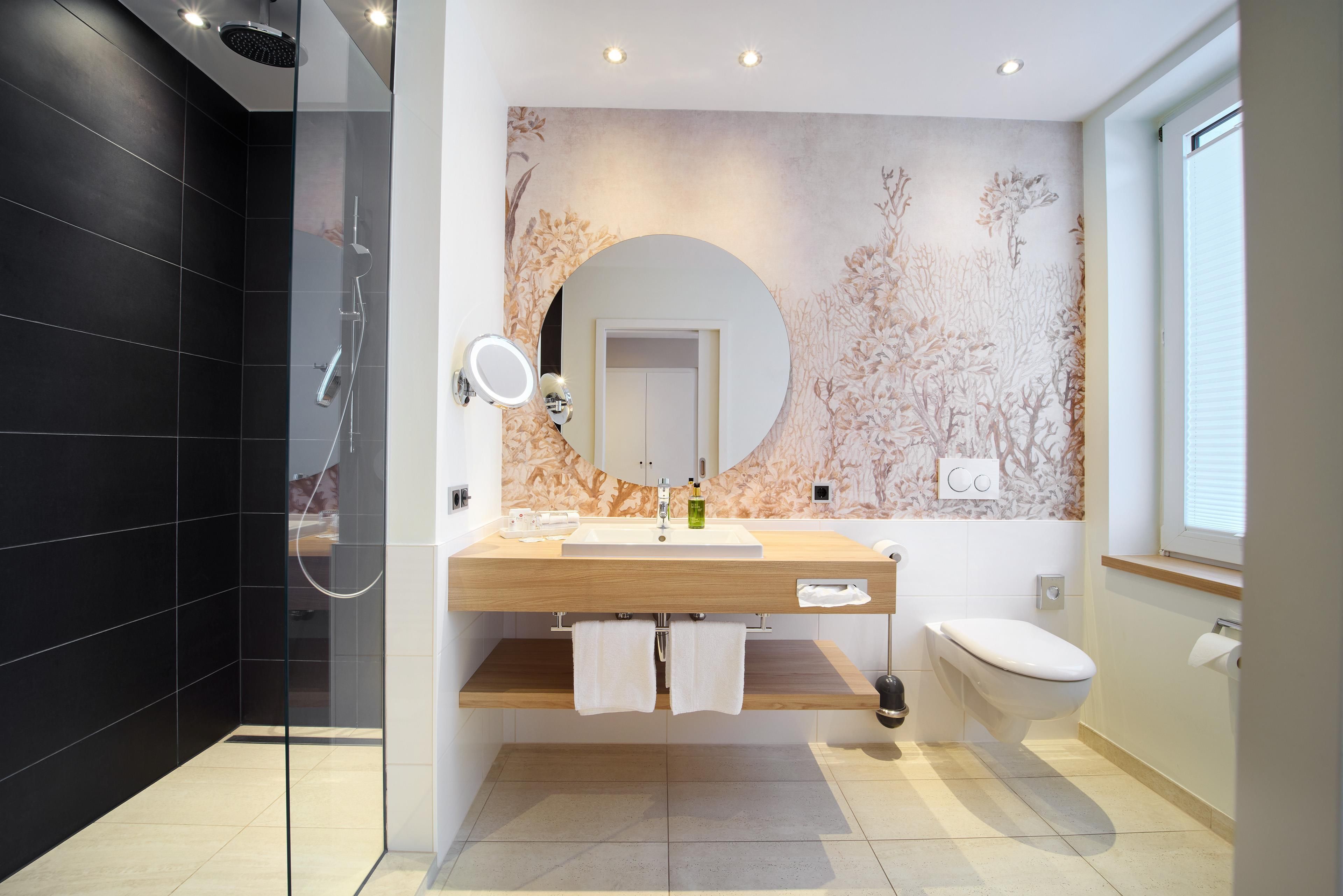Een moderne badkamer met een douchecabine van glas, een houten wastafelmeubel, een toilet en een spiegel bevestigd aan de muur.