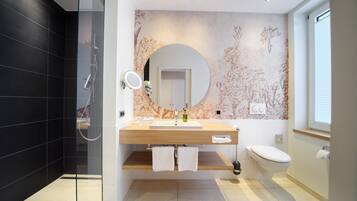 Een moderne badkamer met een douchecabine van glas, een houten wastafelmeubel, een toilet en een spiegel bevestigd aan de muur.