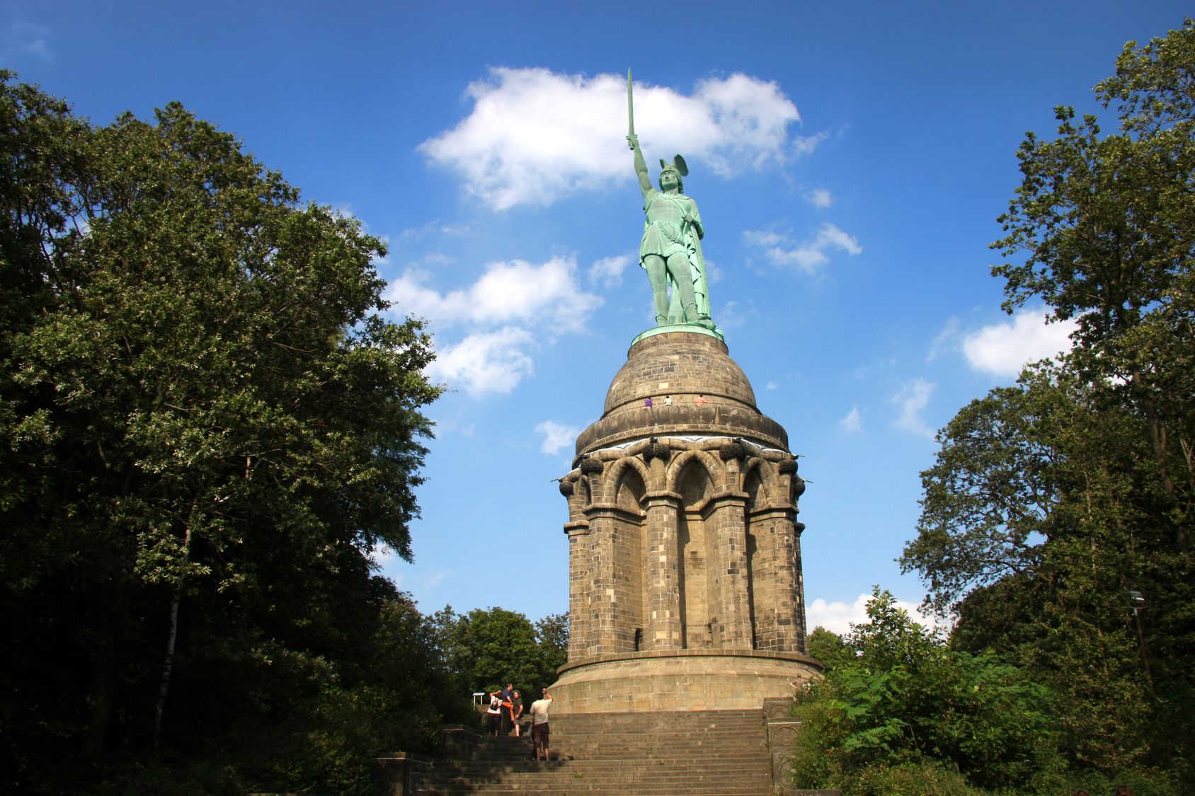 Een standbeeld op een stenen sokkel met een koepel, omringd door bomen.