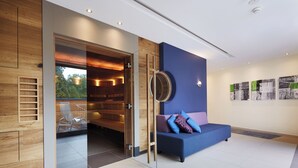 A modern interior with a blue sofa, wooden panel walls, and a glass door leading to a seating area. - Best Western Premier Park Hotel and Spa (Bad Lippspringe)