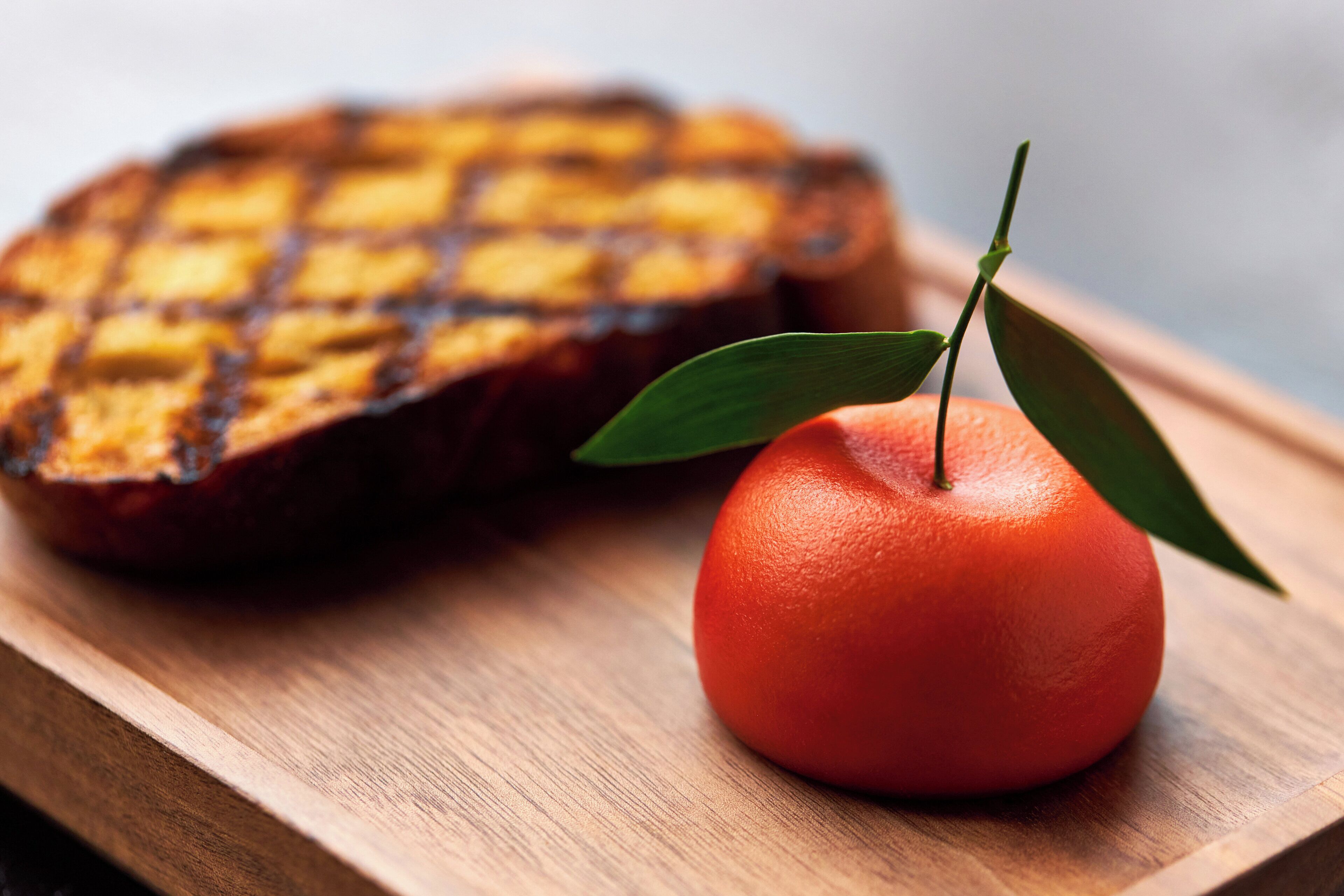 Un sándwich a la plancha y una naranja entera sobre una tabla de madera.