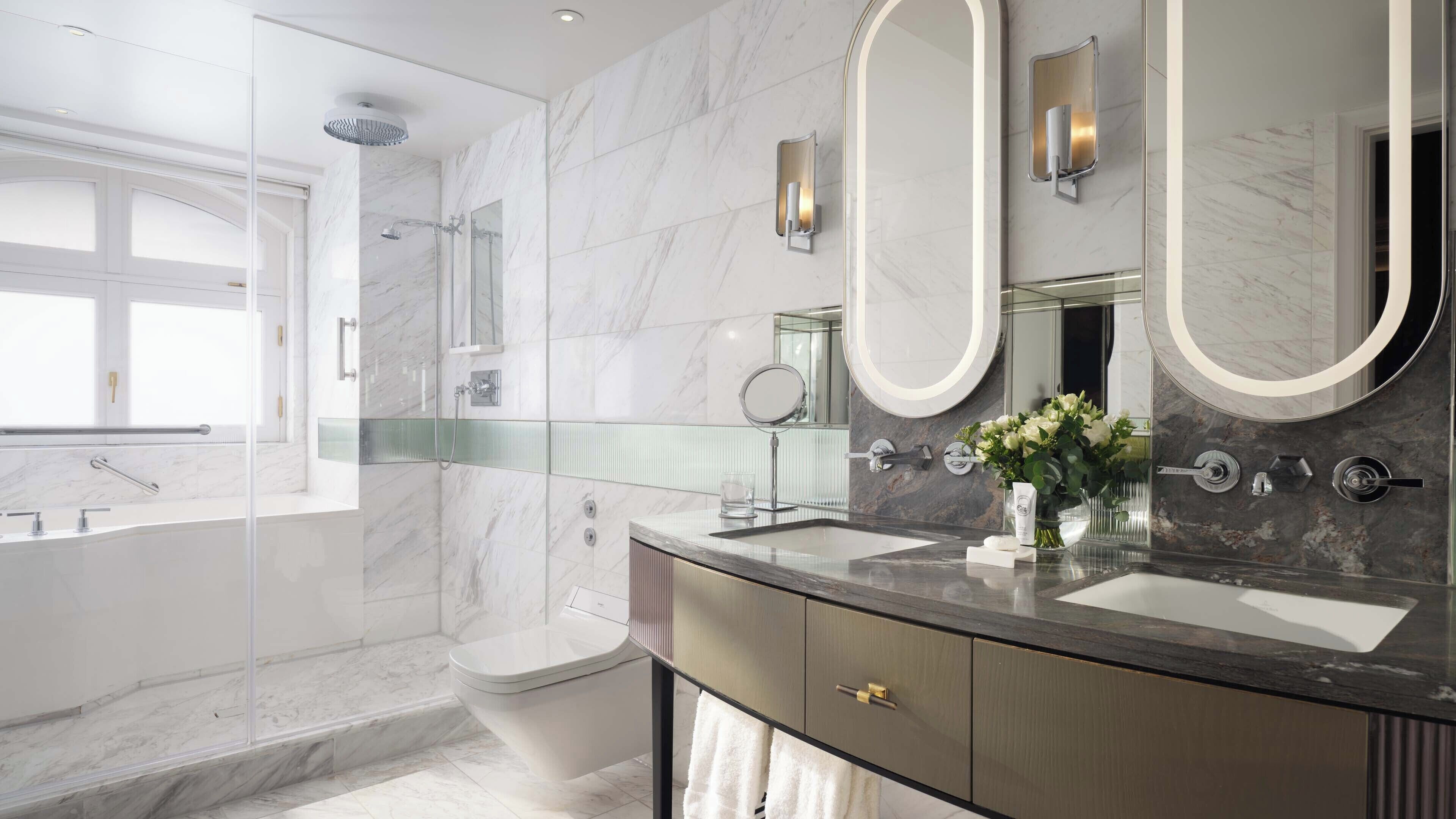 A modern bathroom with a glass shower enclosure, a toilet, a vanity with a large mirror, and a vase with flowers.