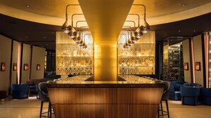 Een bar met een houten toonbank, blauwe zitplaatsen en een behang met een bar op de achtergrond.
