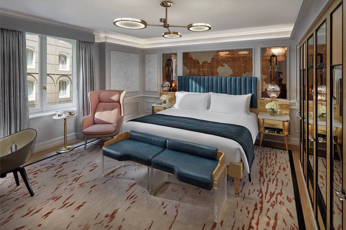 Ein modernes Hotelzimmer mit einem großen Bett, einer Sitzecke, einem Schreibtisch und einem großen Fenster mit Vorhängen.