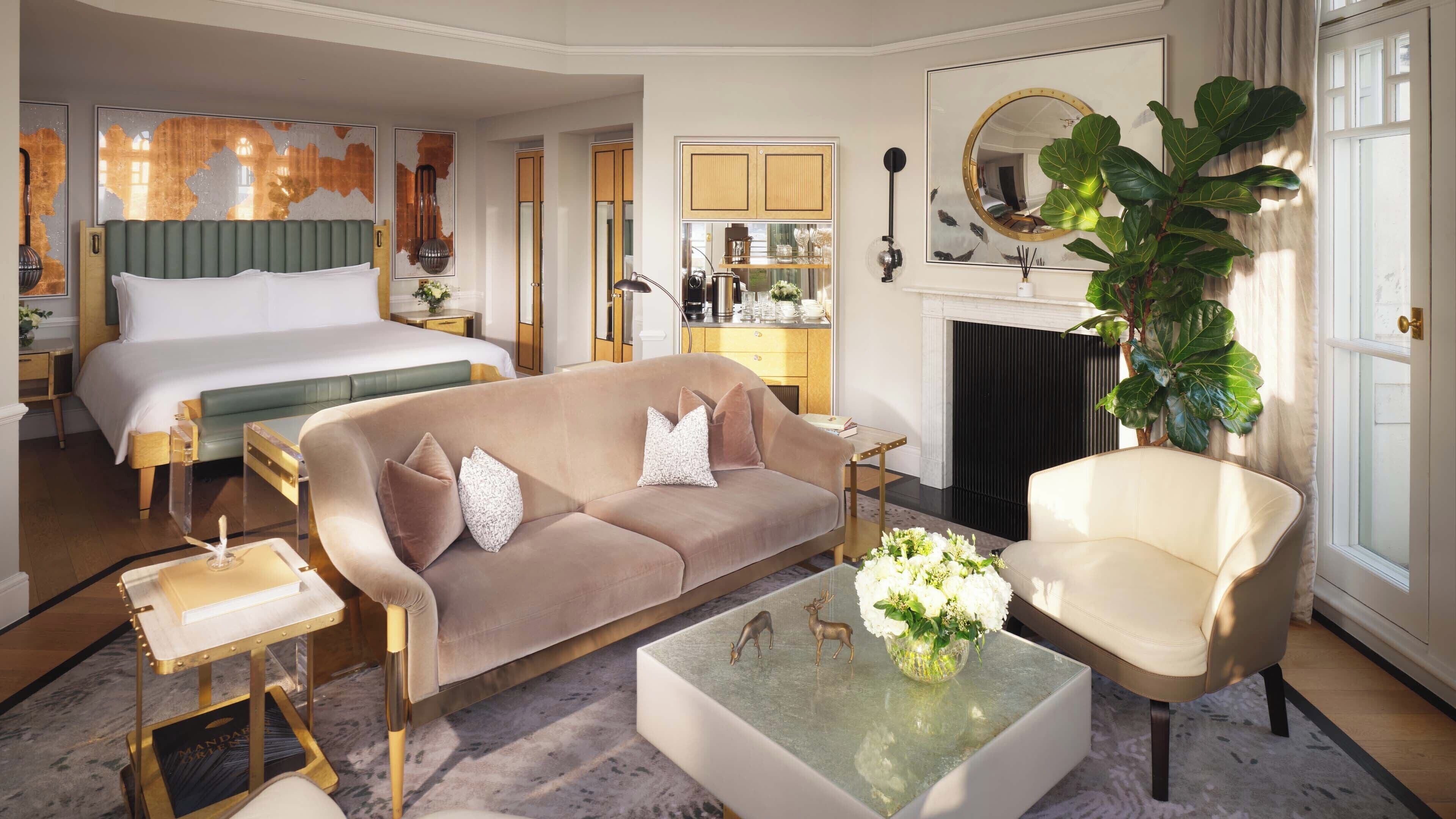 A hotel room with a large bed, a sofa, a chair, a coffee table, and a fireplace.