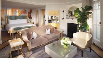 A hotel room with a large bed, a sofa, a chair, a coffee table, and a fireplace.